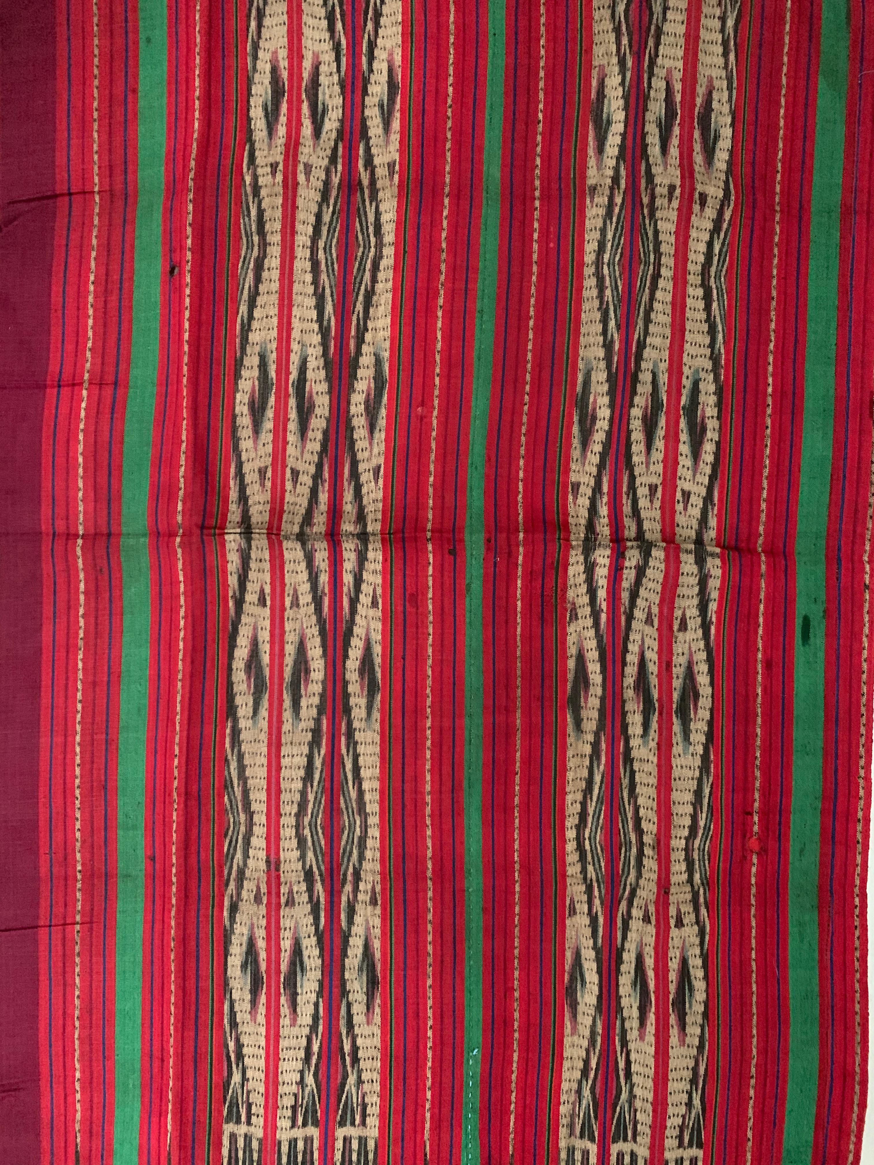 This Ikat textile originates from the Island of Kalimantan, Indonesia. It is hand-woven using naturally dyed yarns via a method passed on through generations amid the Dayak Tribes scattered throughout the island. It features a stunning red, green &