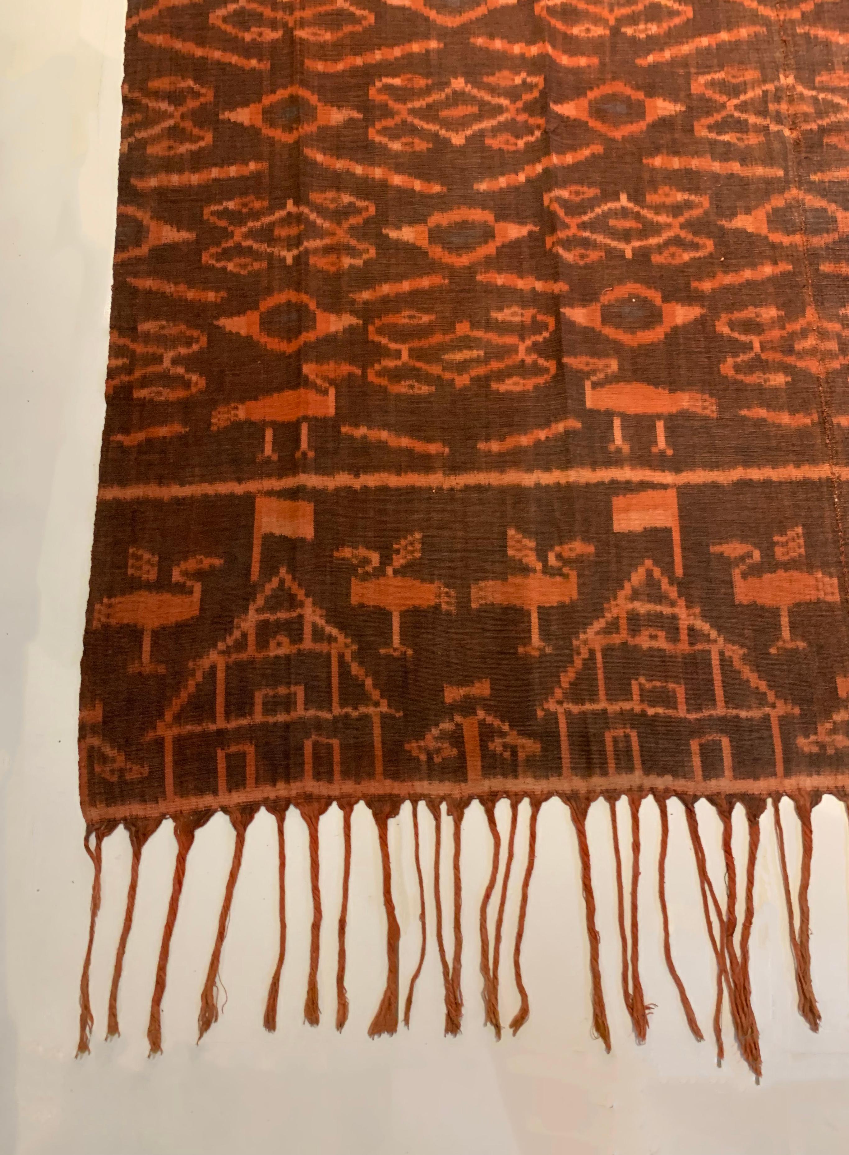 Dieses Ikat-Textil stammt von der Insel Flores in Indonesien. Es wird mit natürlich gefärbten Garnen nach einer seit Generationen überlieferten Methode handgewebt. Es zeigt eine Mischung aus Stammesmustern und der indonesischen Flagge. Es gibt auch