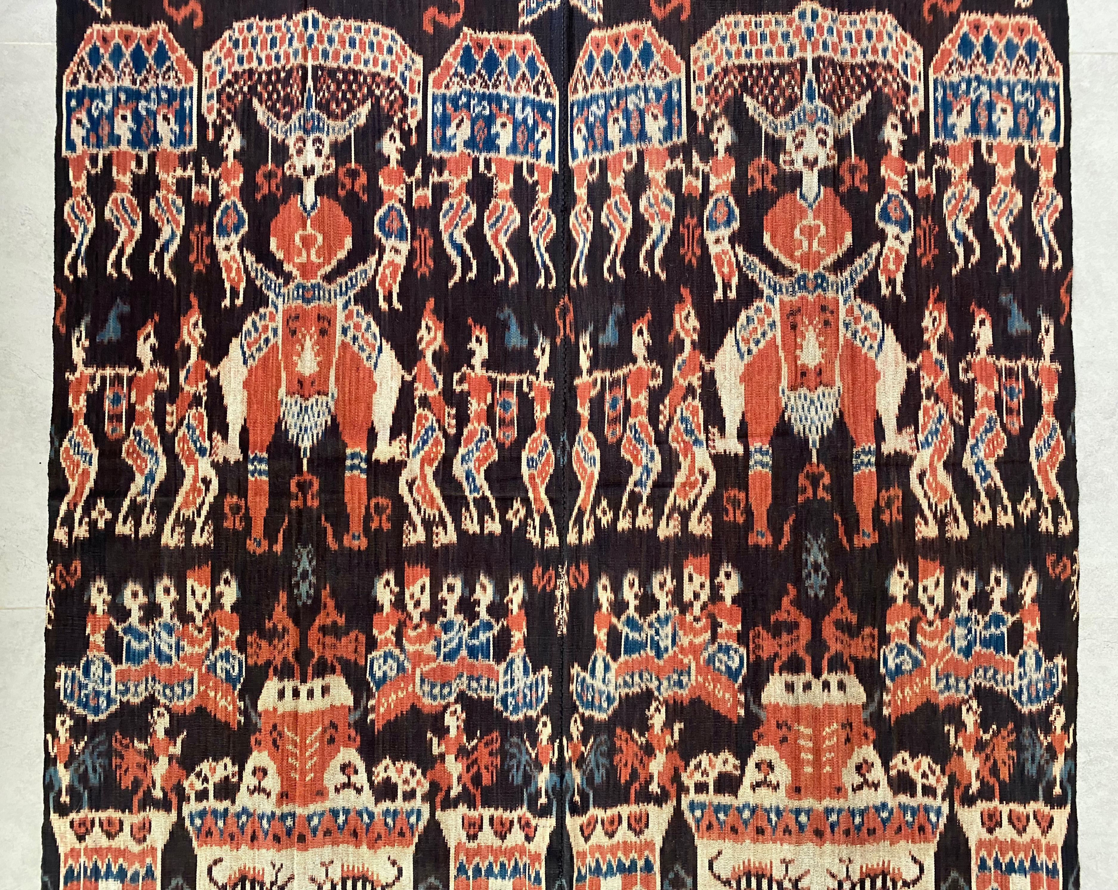 Dieses Ikat-Textil stammt von der Insel Sumba in Indonesien. Es wird mit natürlich gefärbten Garnen nach einer seit Generationen überlieferten Methode handgewebt. Es zeigt einen überwiegend dunkelblauen Hintergrund mit orangefarbenen Verzierungen