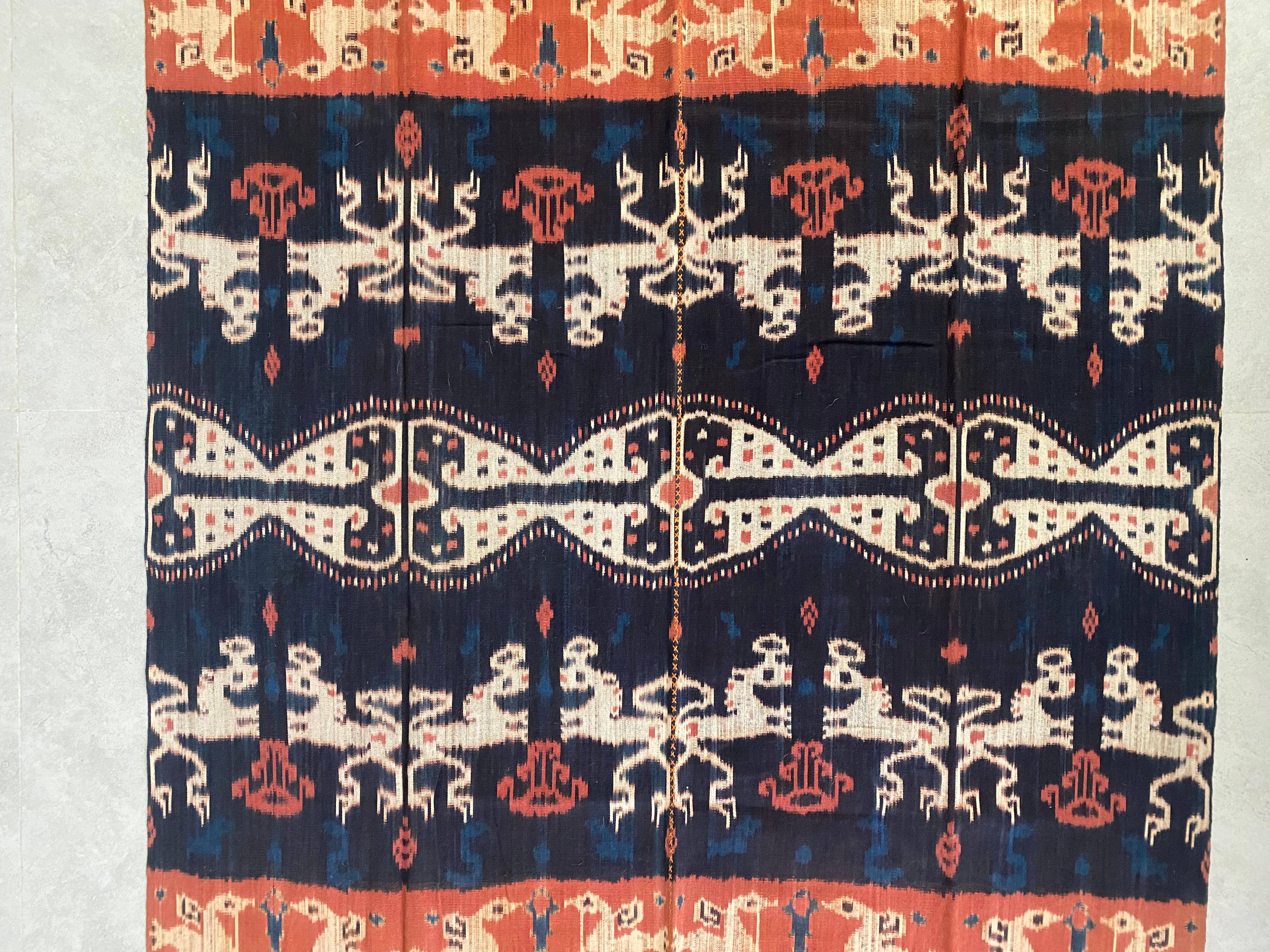 Este tejido ikat es originario de la isla de Sumba (Indonesia). Se teje a mano con hilos teñidos de forma natural mediante un método transmitido de generación en generación. Presenta un fondo predominantemente azul oscuro con detalles de color