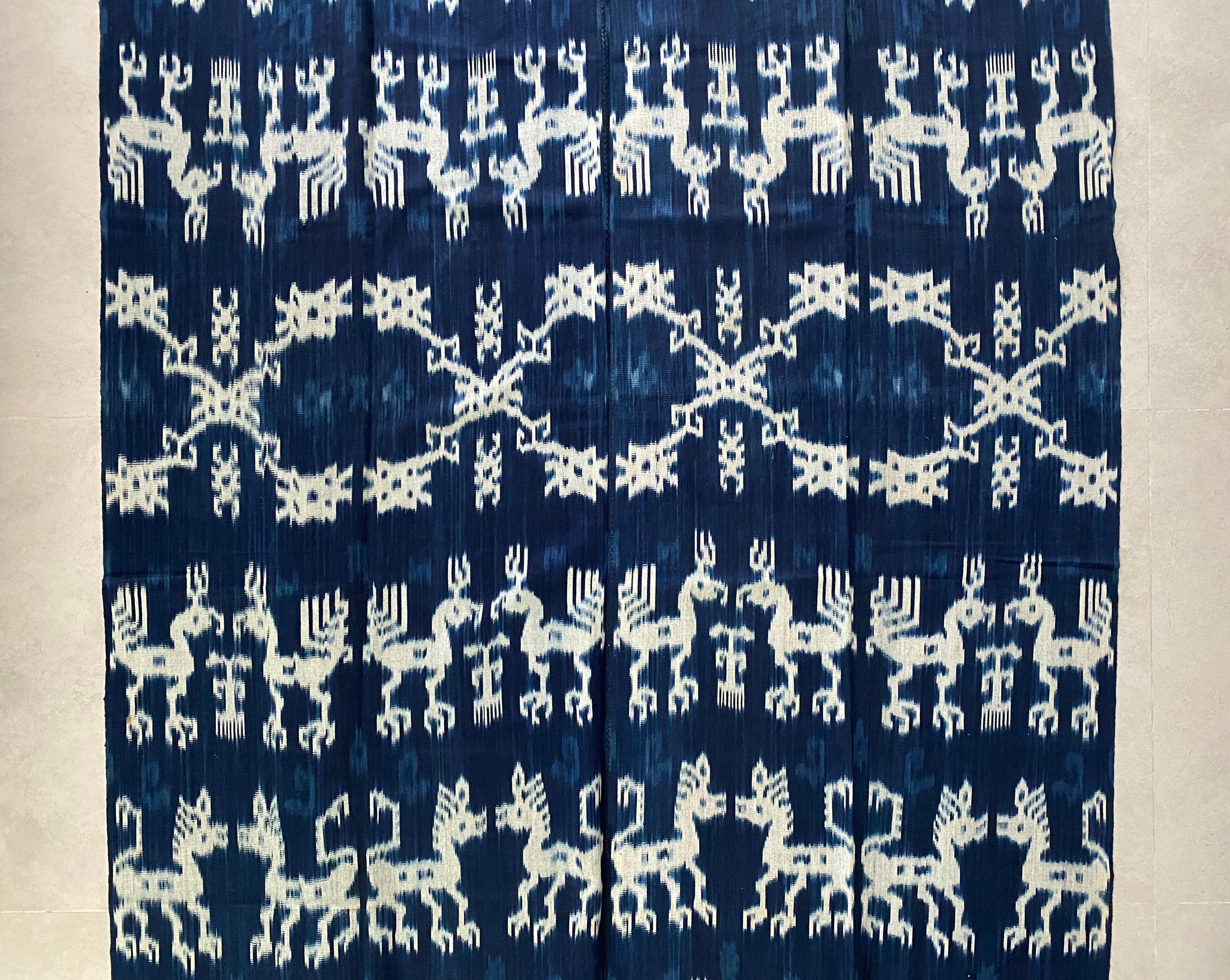 This Ikat textile originates from the Island of Sumba, Indonesia. It is hand-woven using naturally dyed yarns via a method passed on through generations. It features a predominantly dark blue background with chicken motifs and distinct tribal