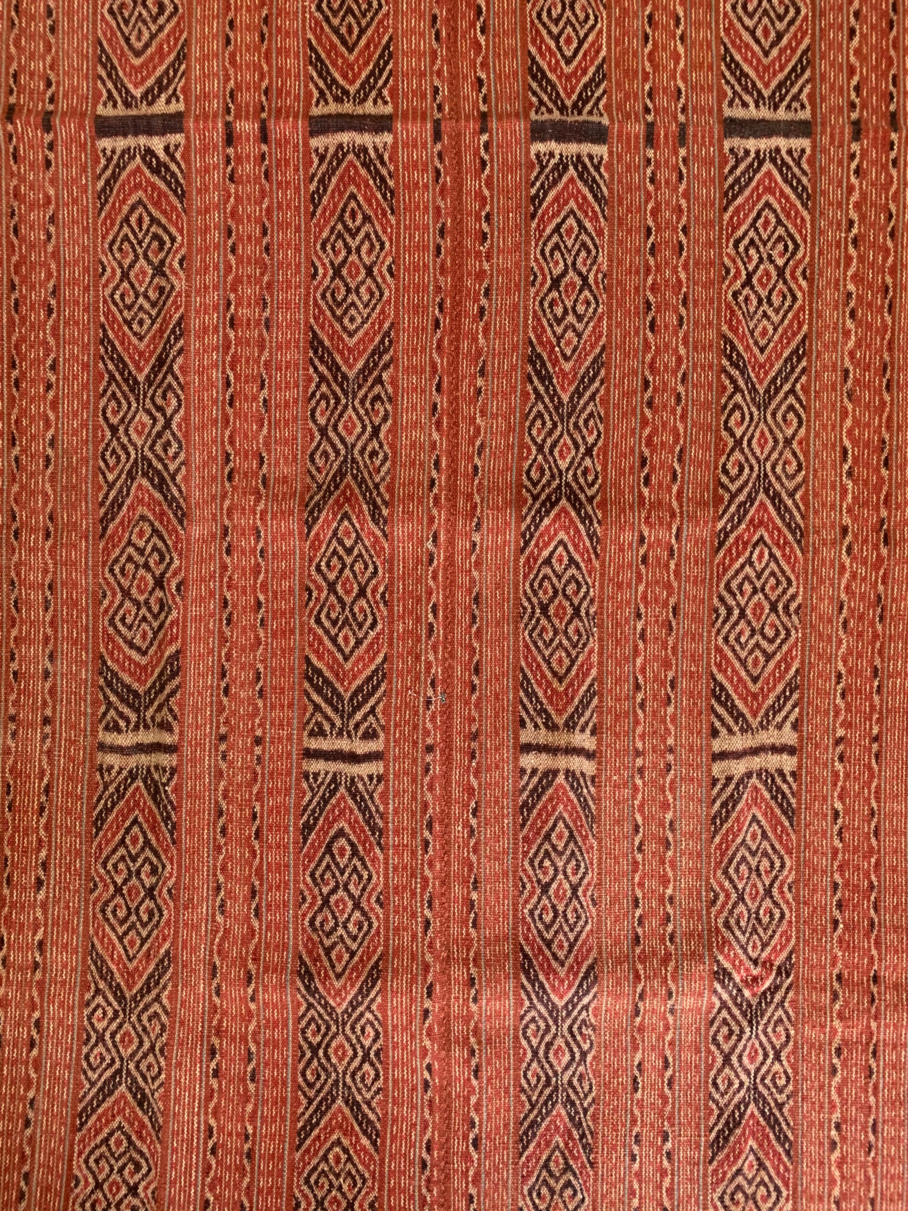 This Ikat textile originates from the Island of Timor, Indonesia. It is hand-woven using naturally dyed yarns via a method passed on through generations. It features a predominantly orange coloured detailing and distinct tribal patterns.