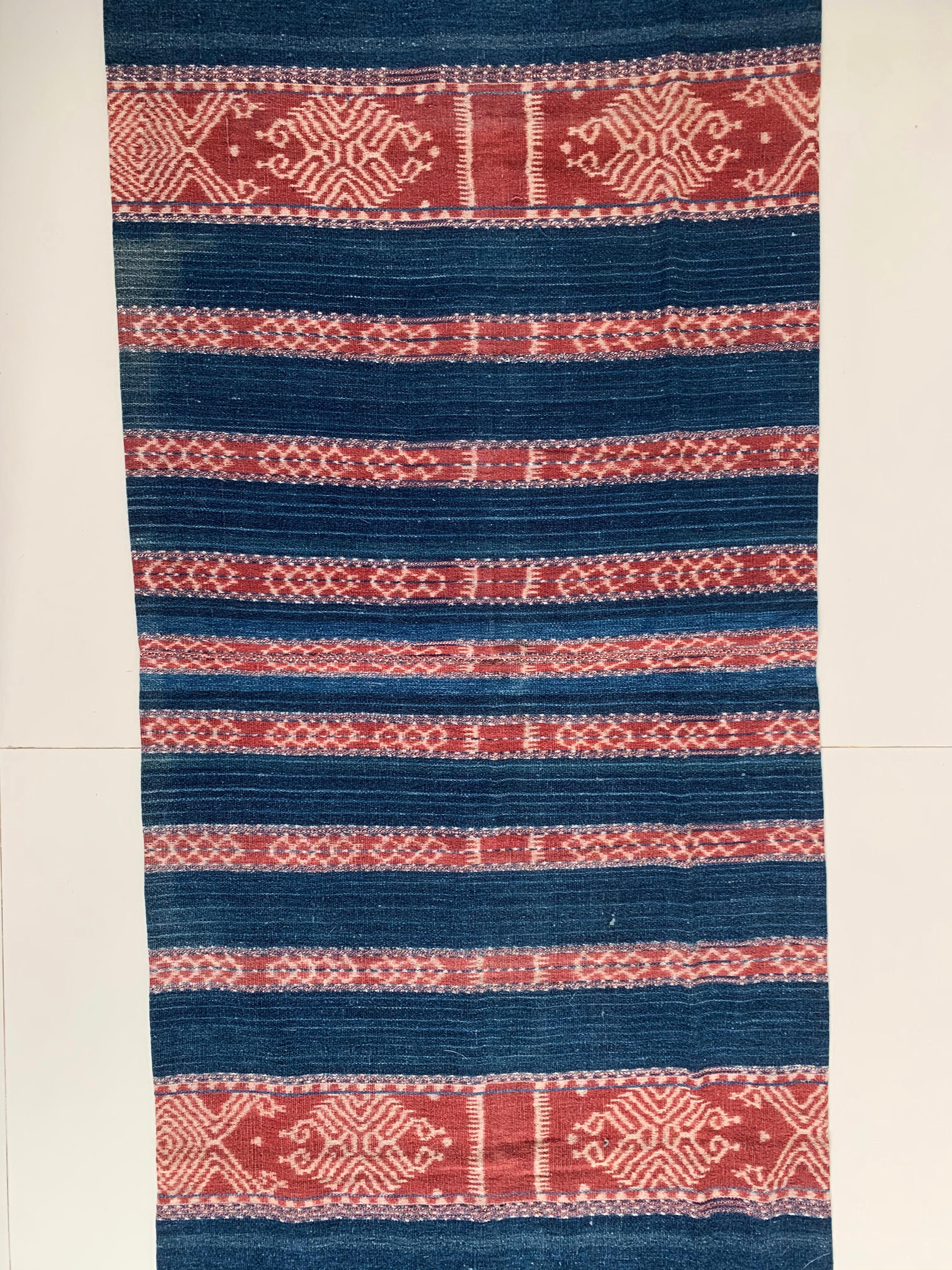 This Ikat textile originates from the Island of Timor, Indonesia. It is hand-woven using naturally dyed yarns via a method passed on through generations. The blue foreground brings to life the array of coloured detailing and distinct tribal