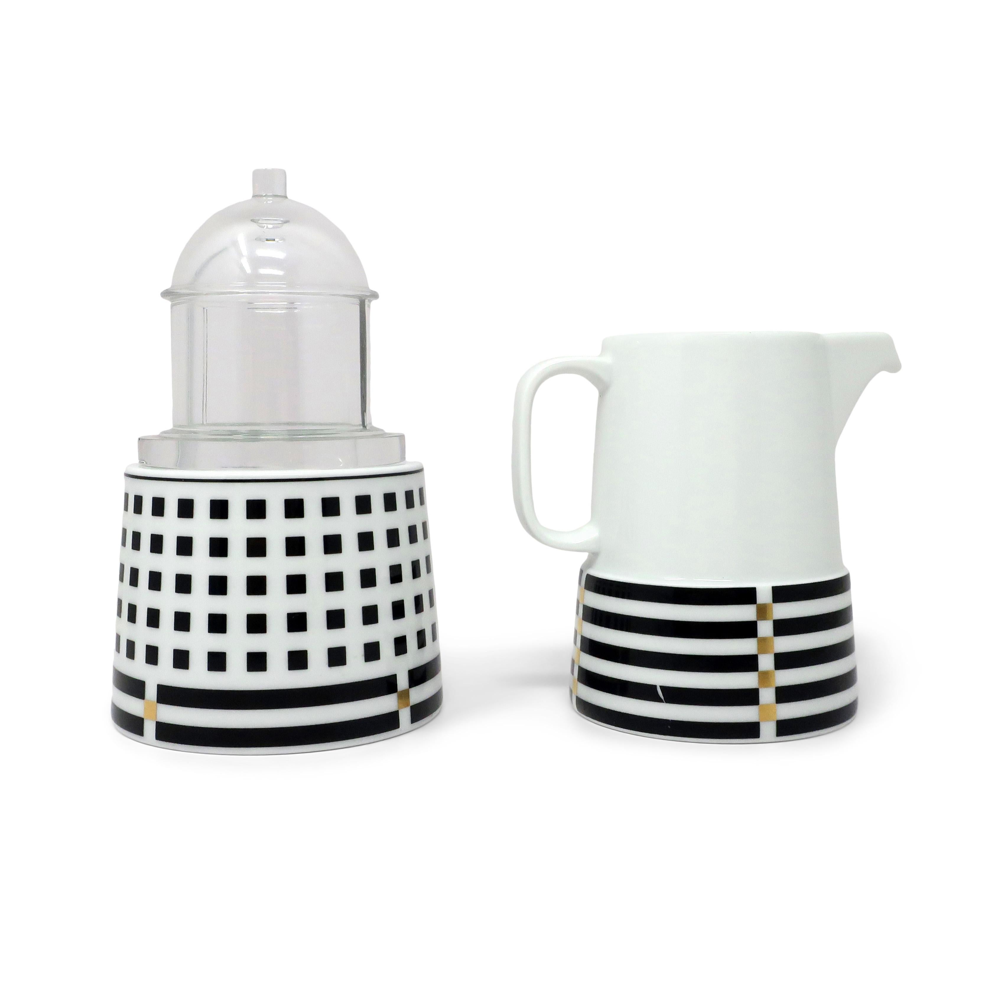 A beautiful set of porcelain creamer and sugar bowl designed by Aldo Rossi for Rosenthal Studio Linie and made in Germany. Both pieces have striped and checkered accents at their base with gold accents and the sugar bowl has a glass top that