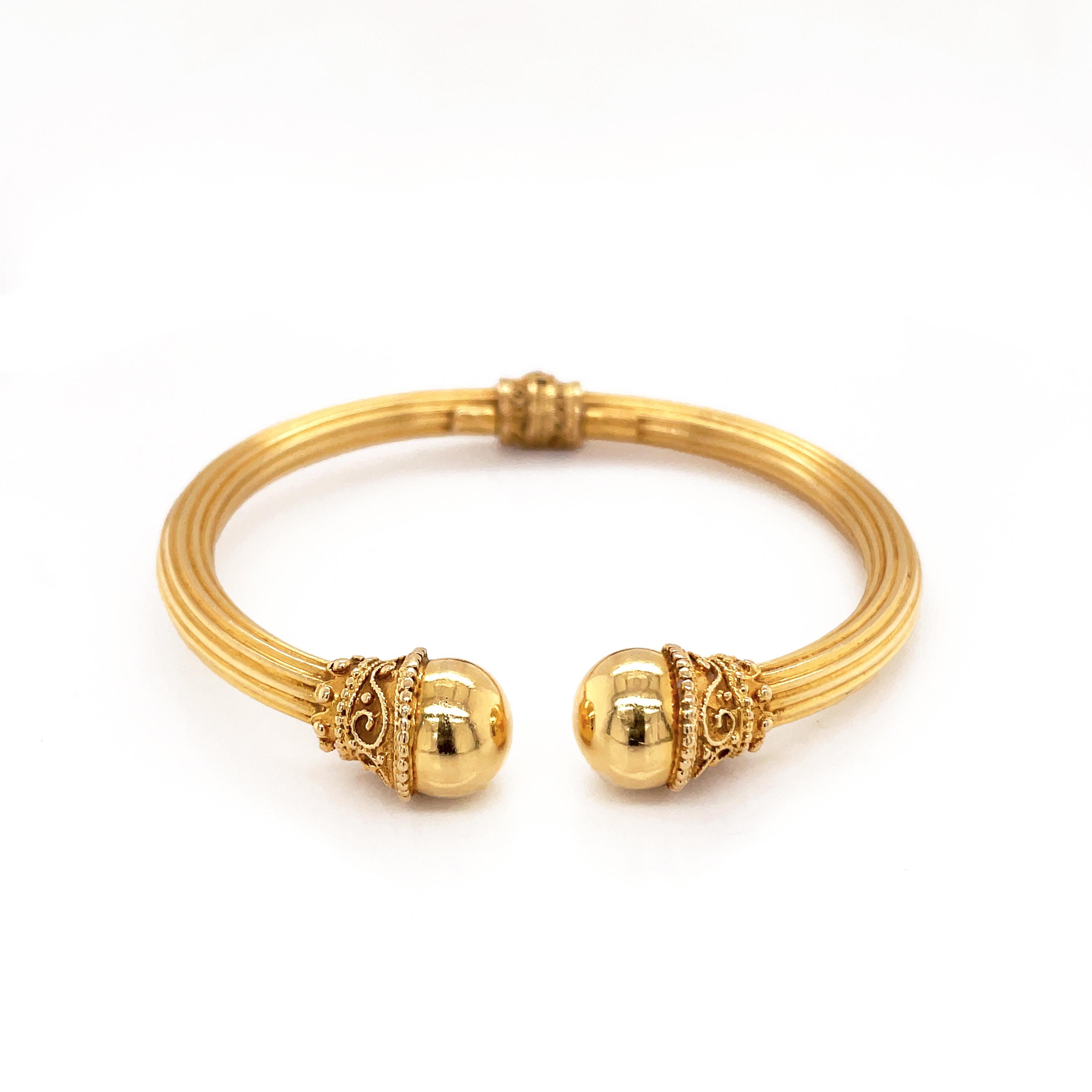 This elegant bangle was created by Greek designer, Ilias Lalaounis for his Hellenistic collection. The bangle is beautifully decorated with ornate raised filigree engraving on either end, holding a smooth sphere and finished with a matching detailed