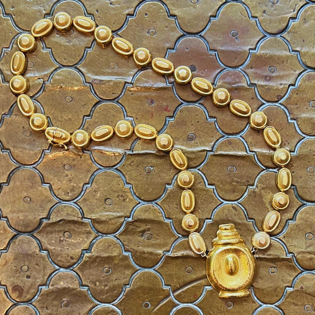 This stunning, handmade 18-karat yellow gold necklace by Ilias Lalaounis, made in 1980 in Greece, features circular and oval links that suspend a hammered gold pendant. Signed “Ilias Lalaounis,” the necklace also bears French import marks for