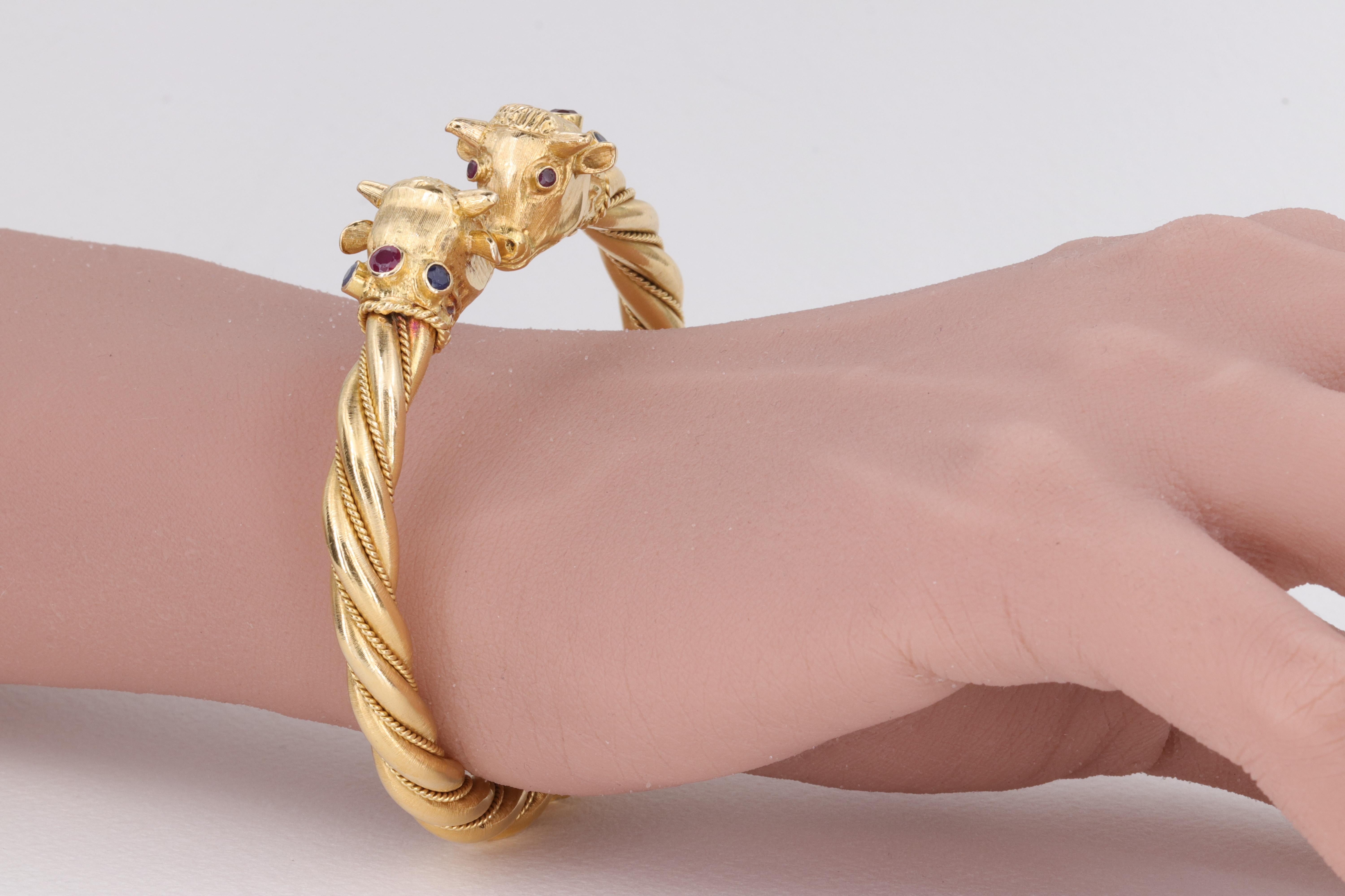 An extremely well made bangle bracelet by iconic Greek jewelry designer Ilias Lalaounis, this bangle depicts 2 Bulls heads atop a textured and twisted 18 karat yellow gold hinged bangle. The bulls are adorned with vivid red ruby eyes, and sapphire &