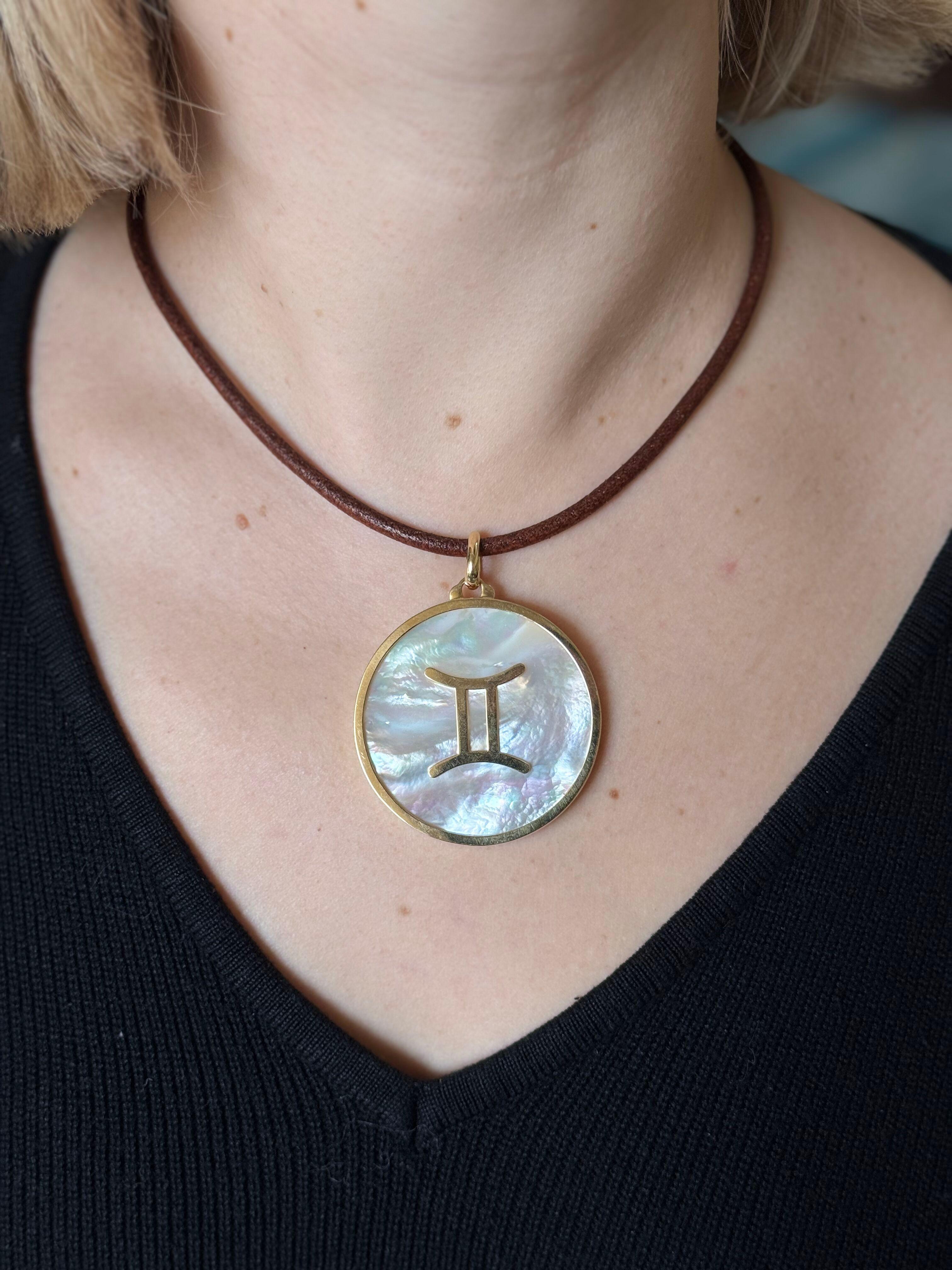 An 18k yellow gold large pendant , by Illario with mother of pearl center, depicting Gemini Zodiac sign. Brown leather cord necklace with 18k gold lobster clasp - 17.25