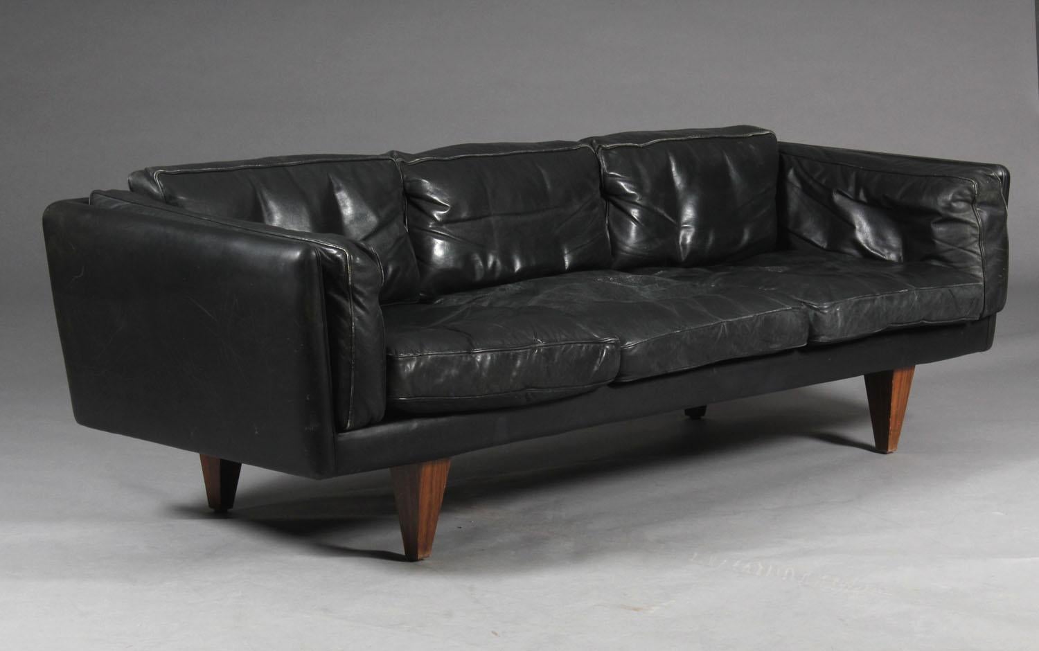 Illum Wikkelso. Three-seater sofa original upholstered with black patinated leather, cone-shaped legs in rosewood. Produced by Holger Kristiansen, 1960s, V11 series.

Illum Wikkelsø. Three-person sofa original covered with black patina
leather,