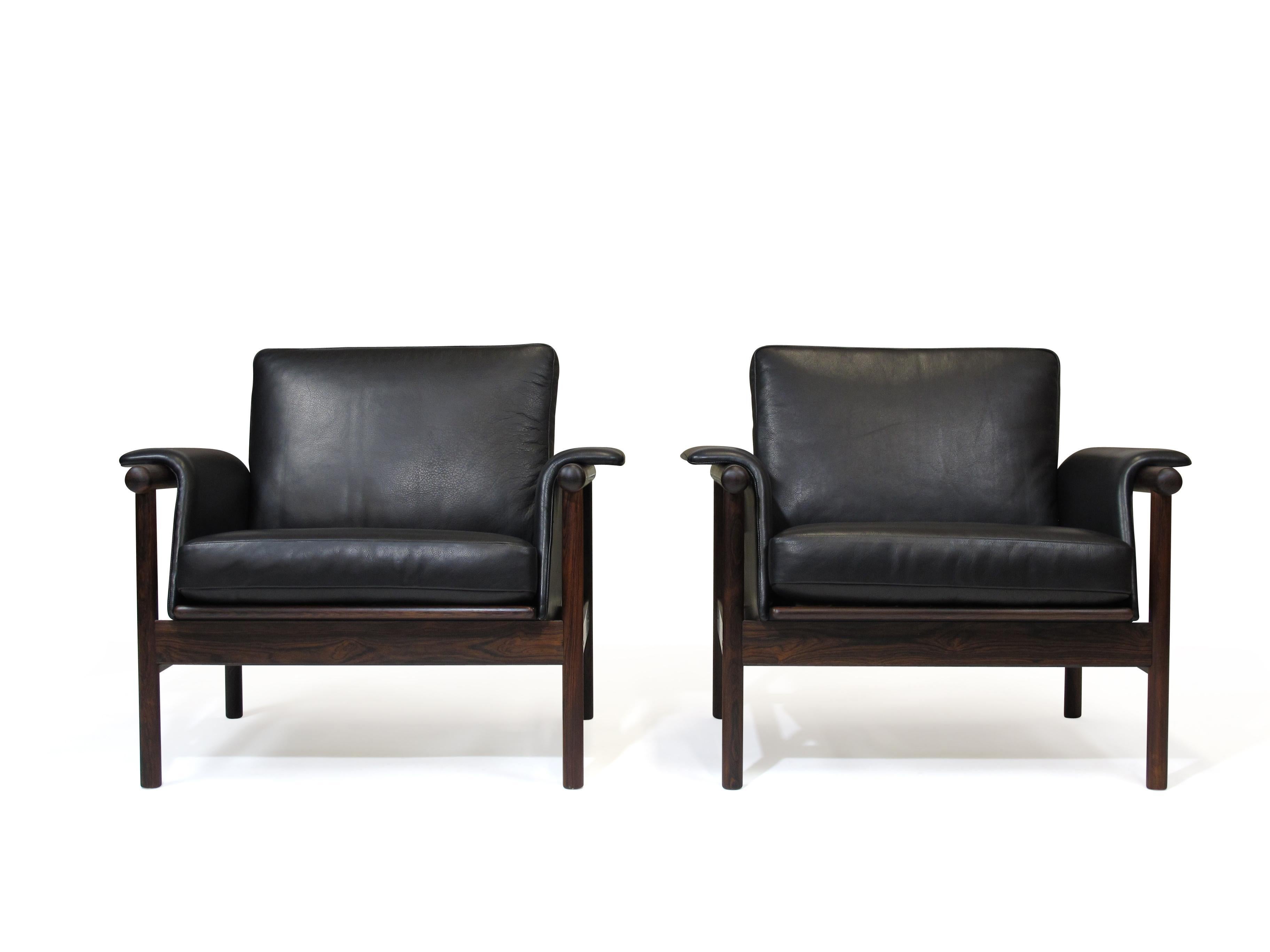 Pair of black leather and rosewood lounge chairs designed by Illum Wikkelsø by Koefoed's Møbelfabrik, Denmark, 1966. Features a solid Brazilian rosewood frame of dark un-faded rosewood, with slatted backrest and slightly rolled arms. Newly