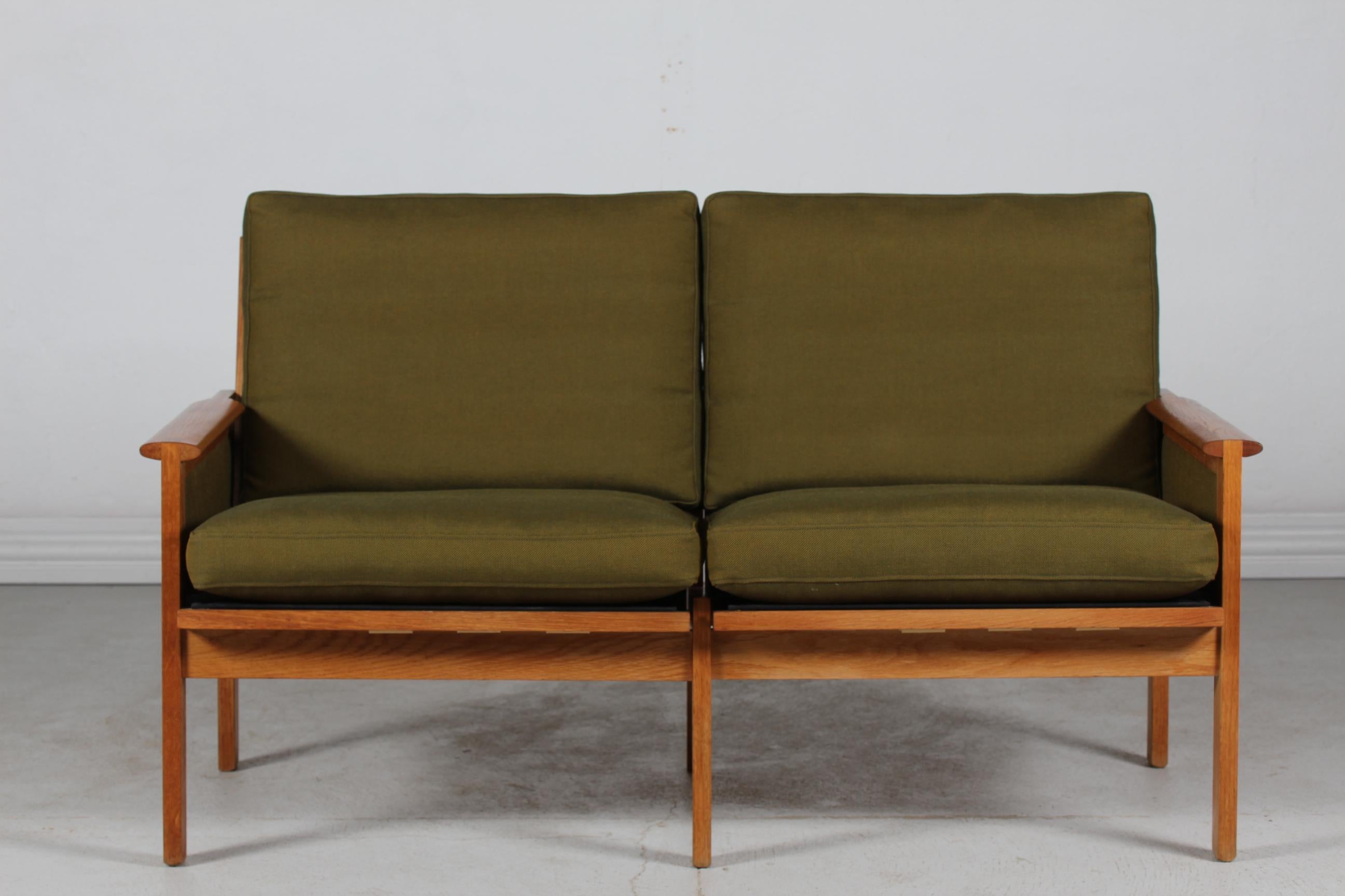 Danish vintage two-seater sofa Capella designed by the Danish furniture designer Kristian Illum Wikkelsø (1919-1999) manufactured by Niels Eilersen, Denmark.
The sofa is made of solid oak and upholstered with the original green colored
