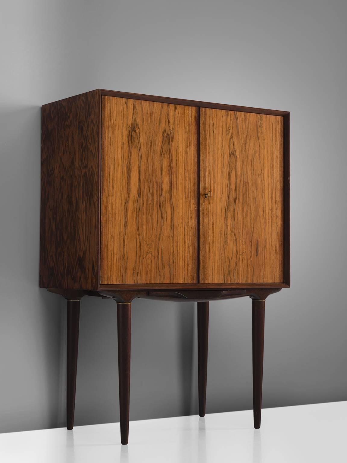 Illum Wikkelsø for C.F. Christensen, rosewood, brass, glass, mirror, Denmark, 1960s.

This elegant high-legged cabinet is designed by Illum Wikkelsø and produced by C. F. Christensen, Silkeborg. The dry bar features cabinet two doors with a key.