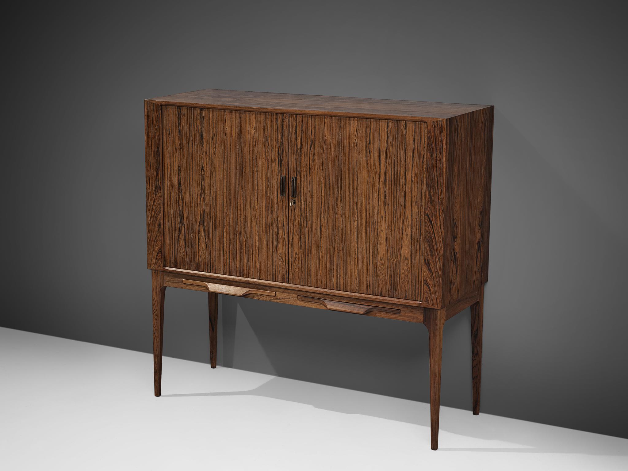 Bar cabinet by Illum Wikkelsø for C.F. Christensen, rosewood, brass, glass, mirror, Denmark, 1960s.

This elegant high-legged cabinet is designed by Illum Wikkelsø and produced by C. F. Christensen, Silkeborg. The dry bar features cabinet two doors