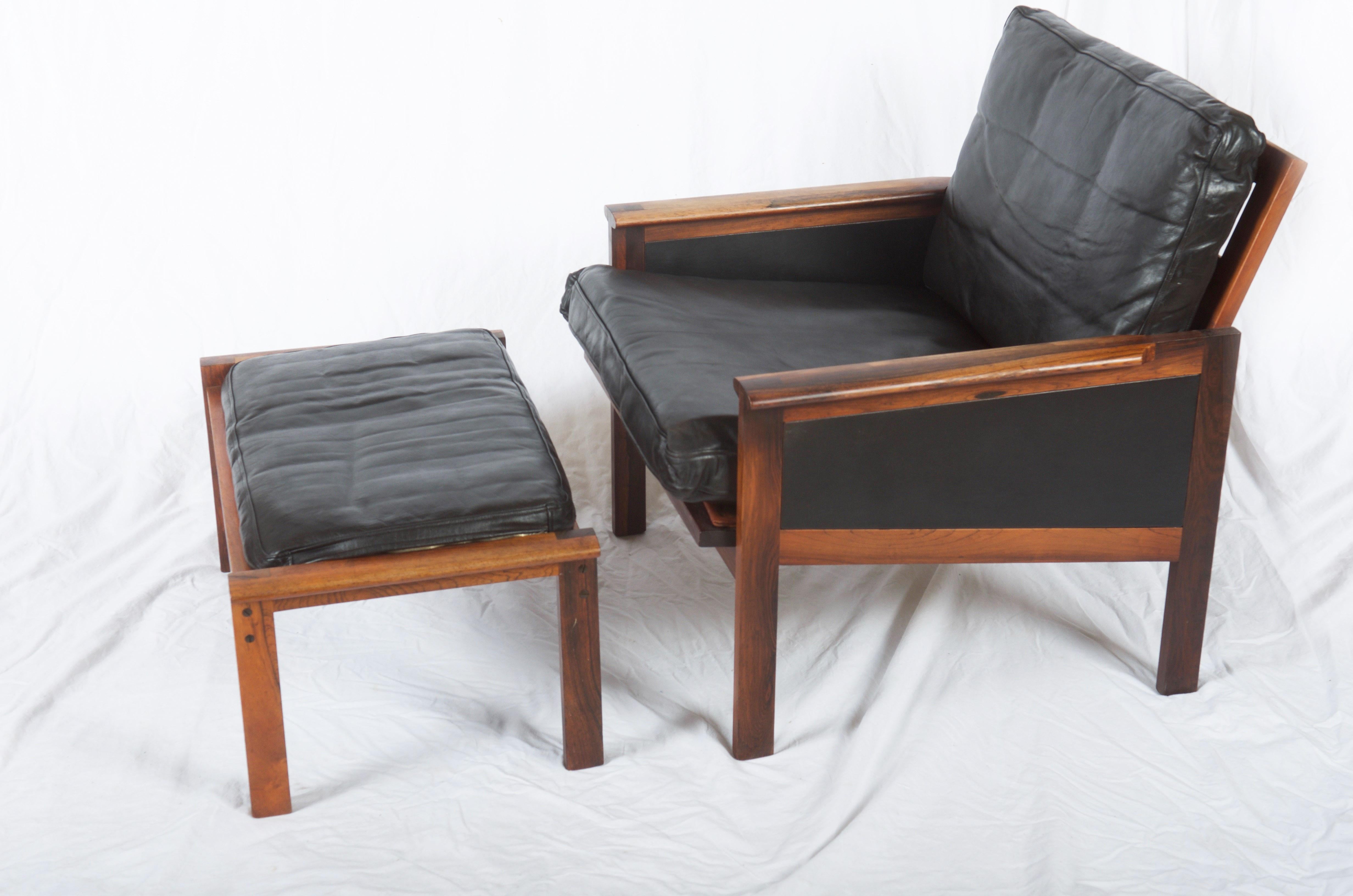 Illum Wikkelsø. Solid hardwood armchair, upholstered in black leather. Related stool H. 35 cm. Manufactured by N. Eilersen, model Capella. Traces of age and wear, including among other things.