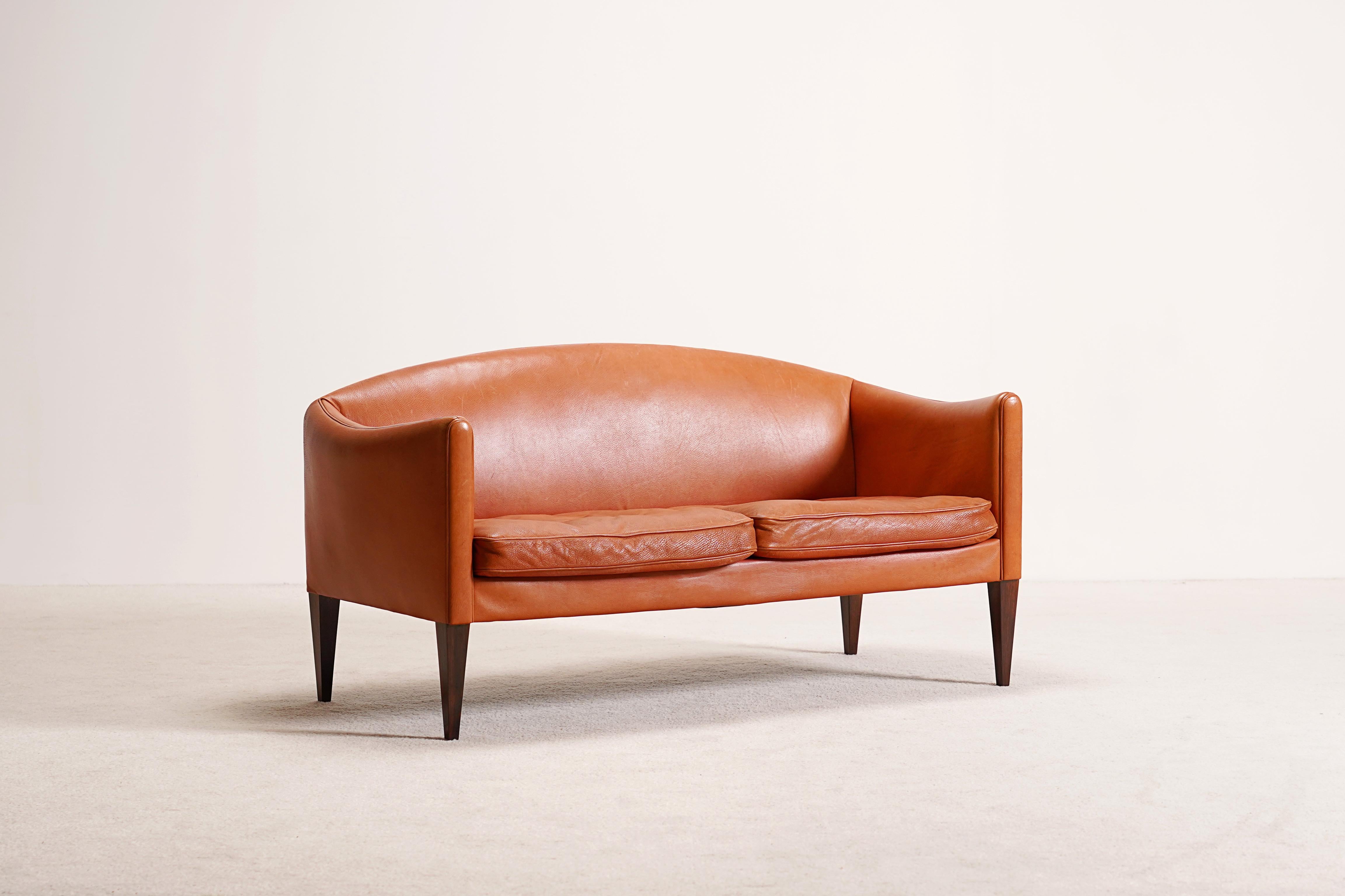 Nice loveseat free-standing sofa Model V12 upholstered in light brown patinated leather, tapered Brazilian rosewood legs.
This very beautiful two-seat sofa was designed by Illum Wikkelsø and produced by Holger Christiansen in the 1960s in