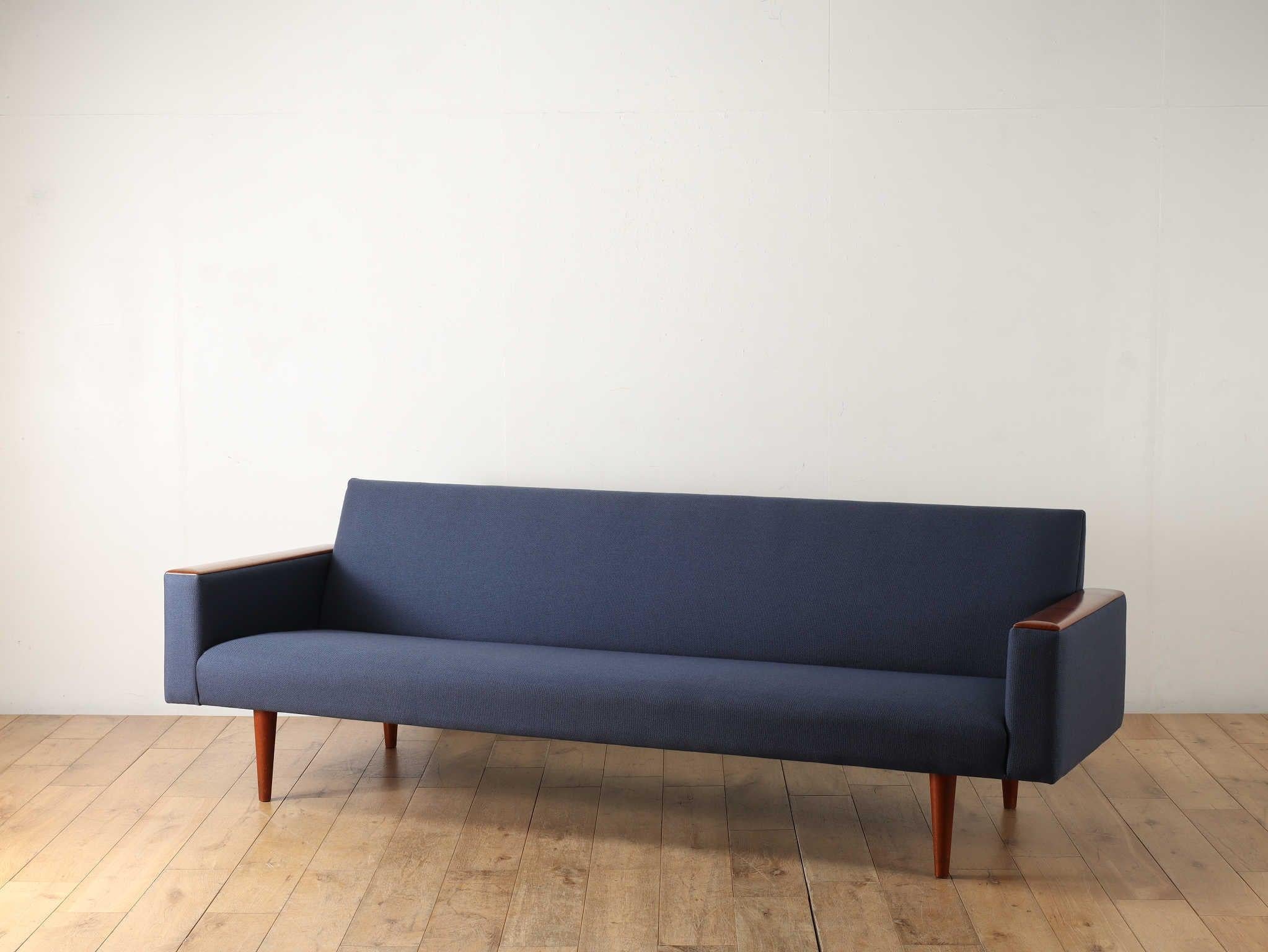 This three-seater sofa was designed by Illum Wikkels. It has a linear and simple form supported by teak legs. The sloping back of the seat and the back part of the sofa are angled to fit easily to the back, creating a comfortable seating experience.