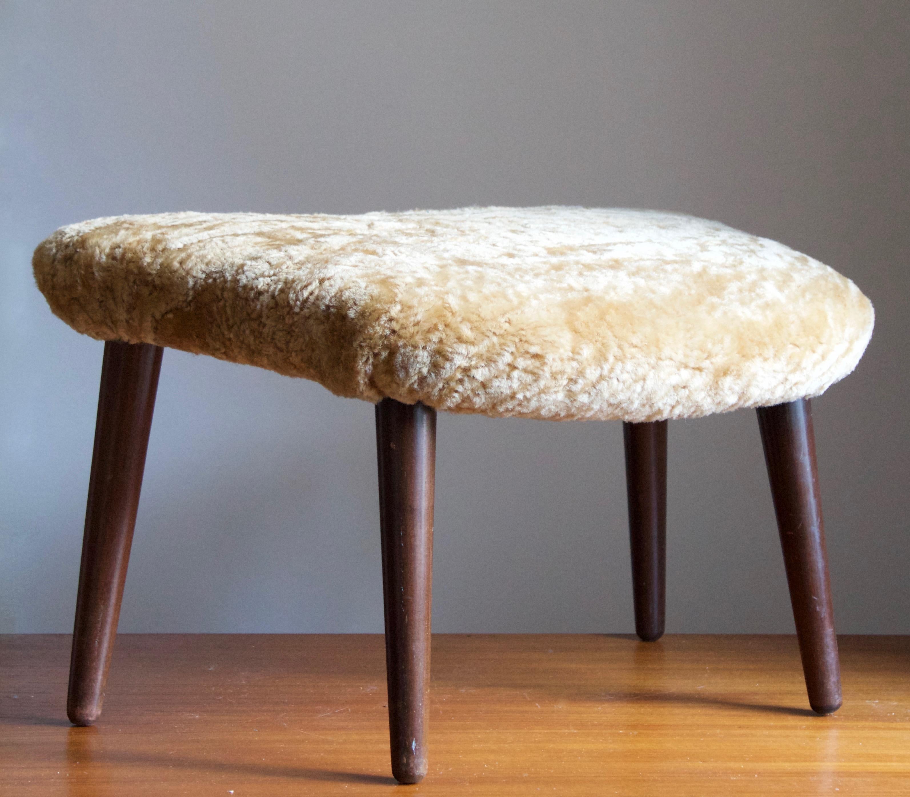 A stool with an organically shaped seat. Designed by Illum Wikkelsø. Solid stained wood, reupholstered in brand new sheepskin. 

   