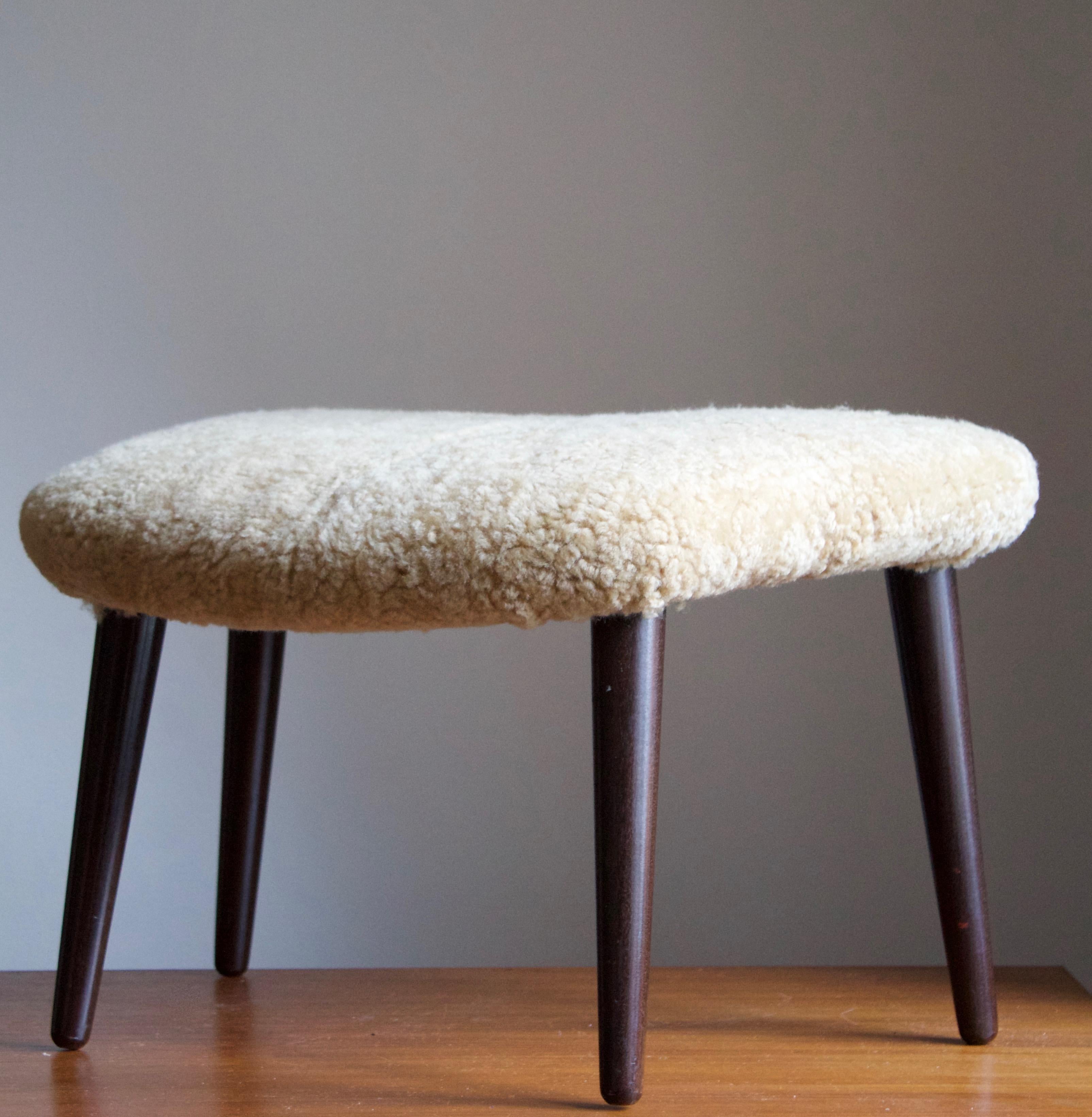 A stool with an organically shaped seat. Designed by Illum Wikkelsø. Solid stained wood, reupholstered in brand new sheepskin. 

 