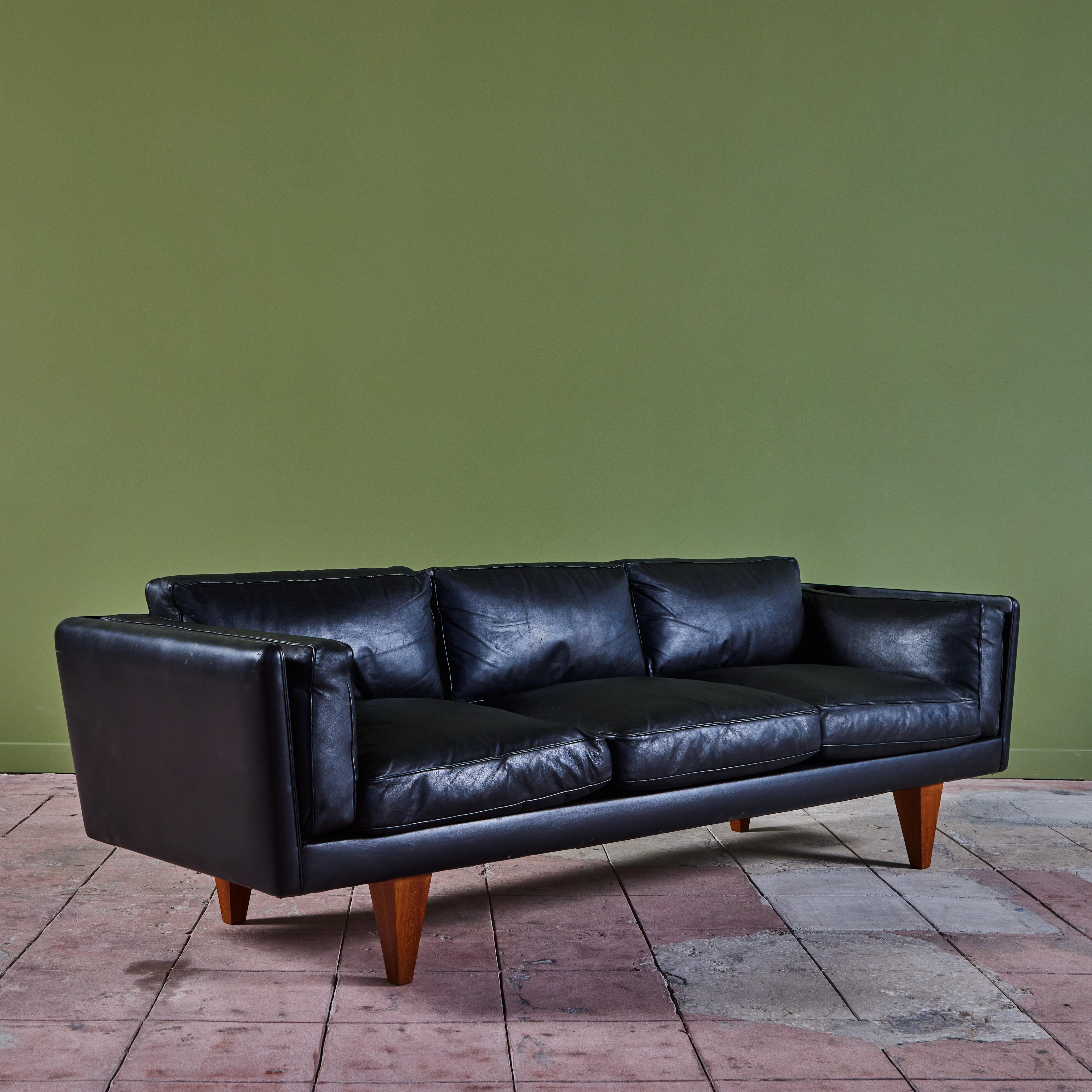 Designed in 1960's by Danish designer, Illum Wikkelsø for Holger Christiansen, this three seater low profile sofa features the original black leather upholstery.  The sofa sits atop four pyramid shaped wooden legs. 

Dimensions
90” width x 33” depth