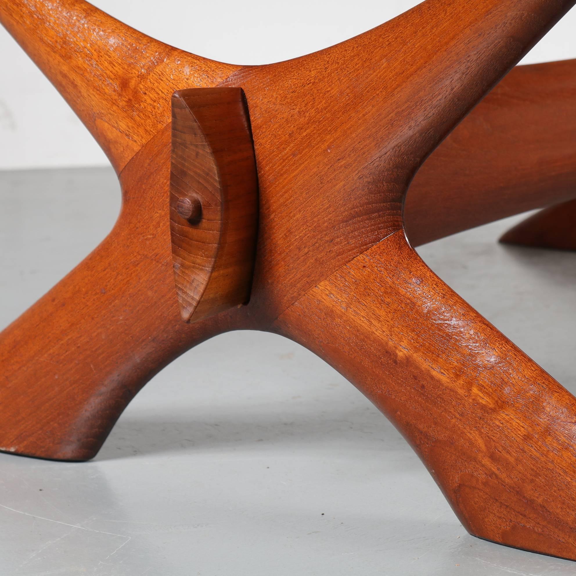 This very elegant coffee table is designed by Scandinavian designer Illum Wikkelso and manufactured by C.F. Christiansen in Denmark, circa 1950.

It has a eye-catching teak wooden base in a smooth, X-shaped design with a horizontal bar for extra