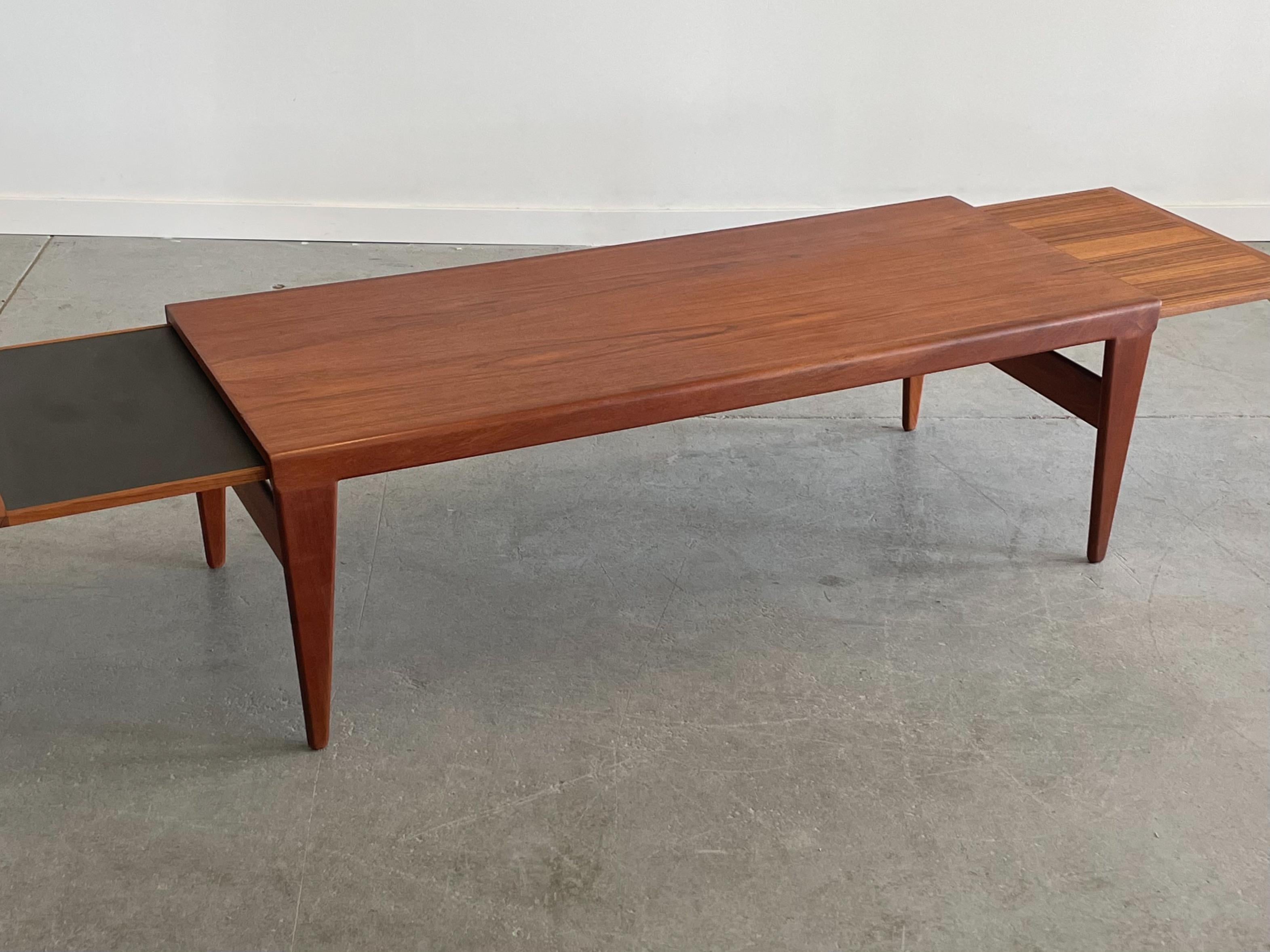 Expanding teak coffee table designed by Illum Wikkelso for Koefoeds, Denmark. This piece features a substantial and beautifully sculpted profile with nicely tapered legs. There is a pull-out for expansion on each side, one with black laminate.