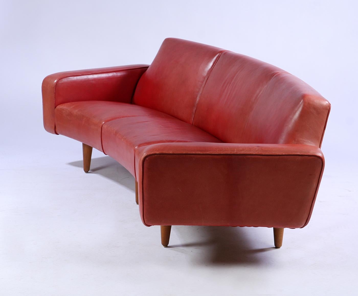 Designed by Illum Wikkelso and made by Aarhuspolstermobelfabrik in the 1960s, this curved sofa retains its original red leather and a matching coffee table. As shown in the scanned advertisement from the 1960s, the coffee table fits nicely with the