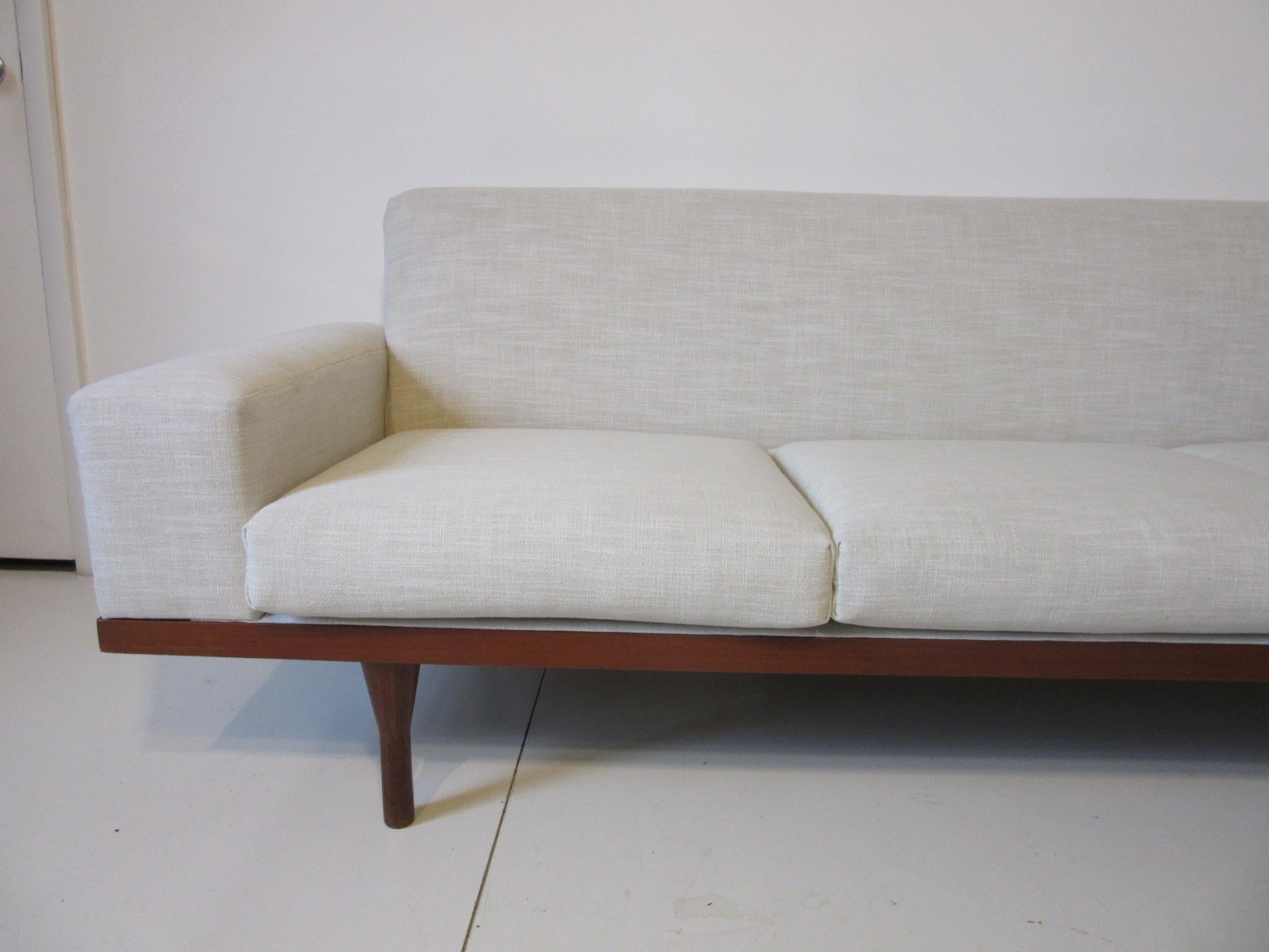 An upholstered sofa or loveseat with three lose bottom cushions all refinished in a woven creamy white and beige fabric. The solid teak frame has removable solid teak legs and is well constructed by early Danish crafts persons in 1962. Made in
