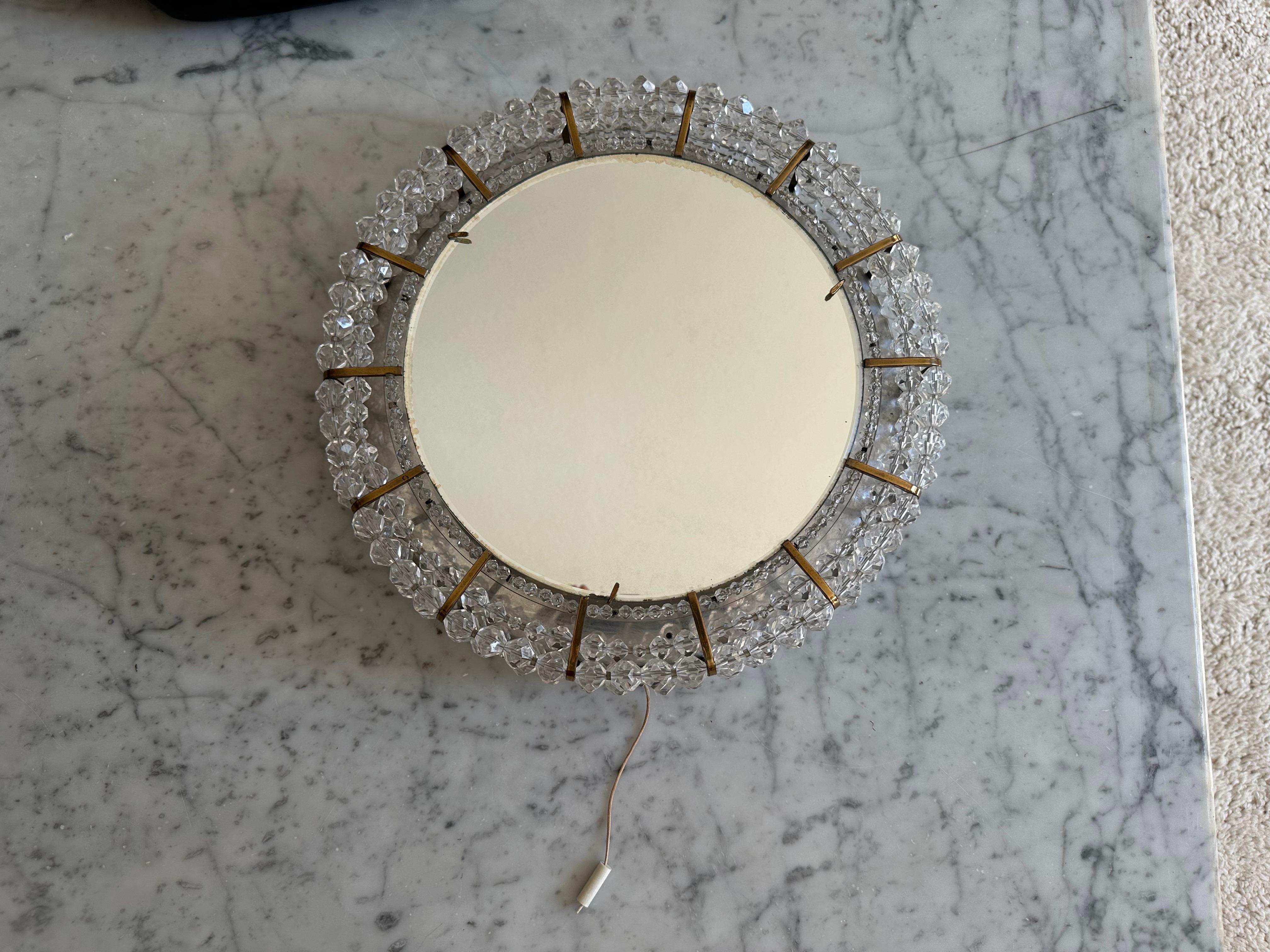
Ce miroir mural rond, rare et rayonnant, a été conçu par Emil Stejnar pour Rupert Nikoll en Autriche dans les années 1950. Stejnar est célèbre pour ses luminaires romantiques, presque magiques, qui combinent souvent le laiton, de délicates fleurs