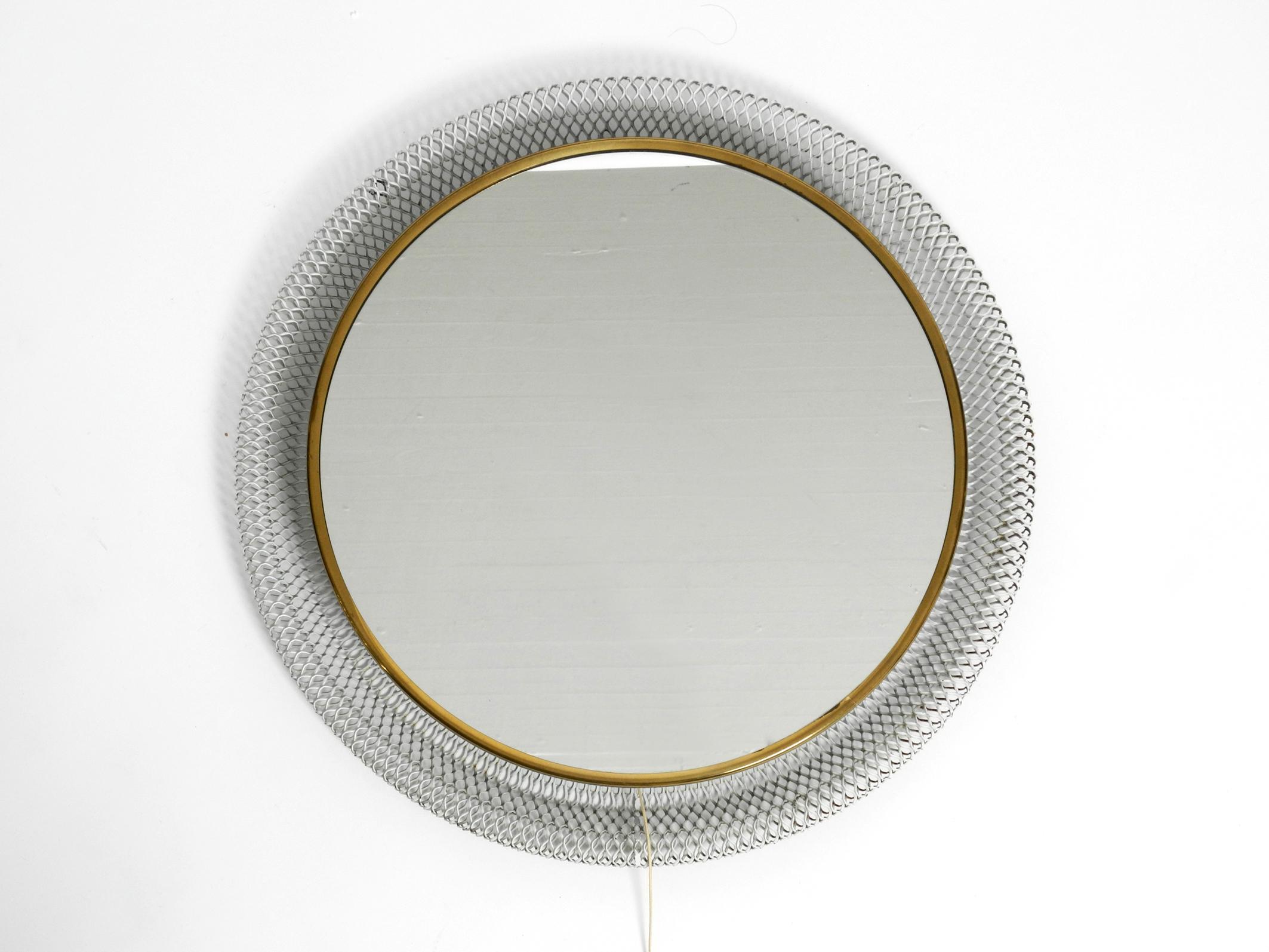Beautiful round backlit Mid-Century Modern wall mirror with white expanded metal frame and brass rim.
Fantastically beautiful 1950s design in a good vintage condition.
Behind the mirror glass are three E14 sockets for 40W each.
With cable switch