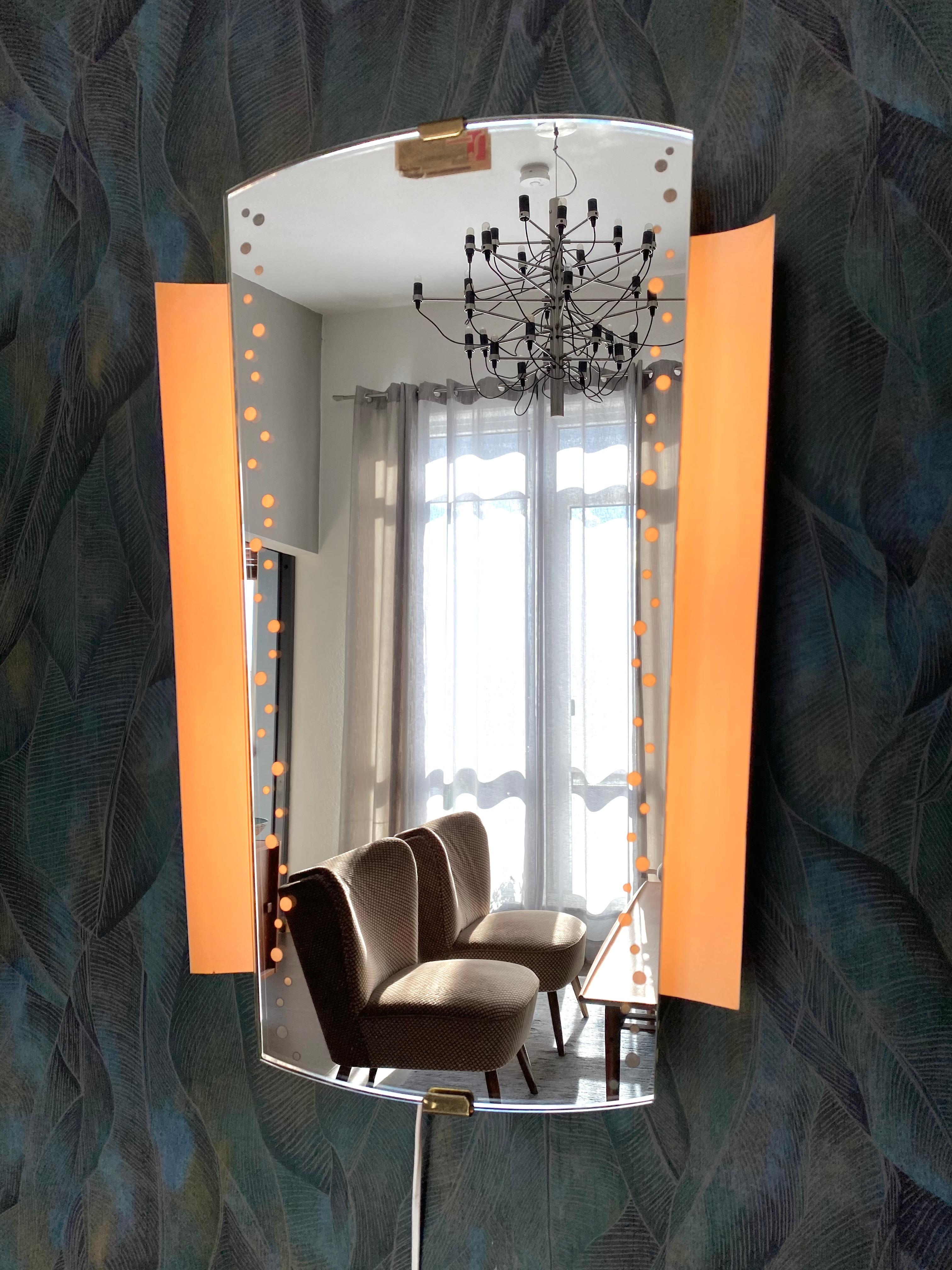 A wall mirror with indirect lighting from the German manufacturer Hillebrand Lighting. It was manufactured in the 1960s. The frame contains four E27 bulbs (max. 40W). The mirror frame and base are made of metal.

This vintage item is fully