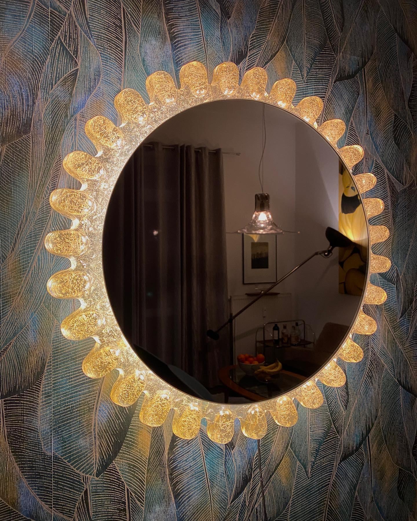 A wall mirror with indirect lighting from the German manufacturer Hillebrand Lighting. It was manufactured in the 1970s. The mirror screws onto the metal backplate to allow access to the bulbs. Perfect for a dressing room, bedroom, or living room to