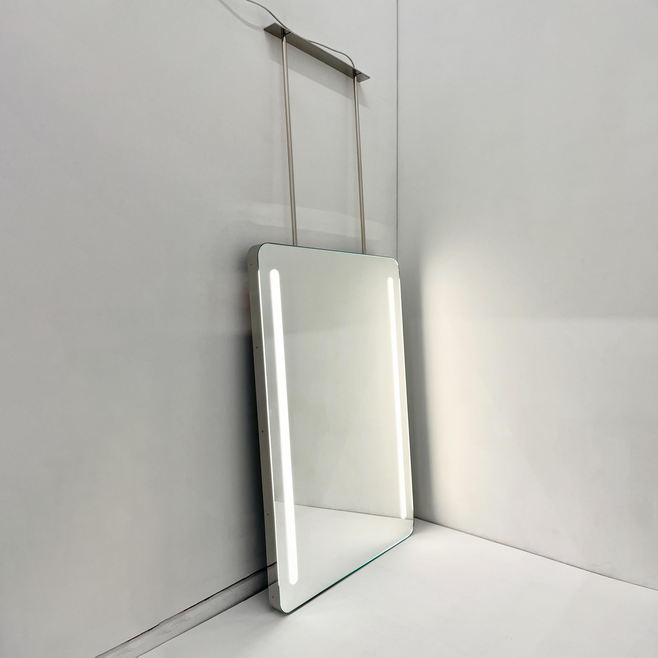 Magnifique miroir rectangulaire moderne avec un cadre en acier inoxydable poli et un éclairage frontal.  Cette pièce fait partie de notre collection originale et entièrement personnalisable de miroirs suspendus au plafond, conçus et fabriqués à la