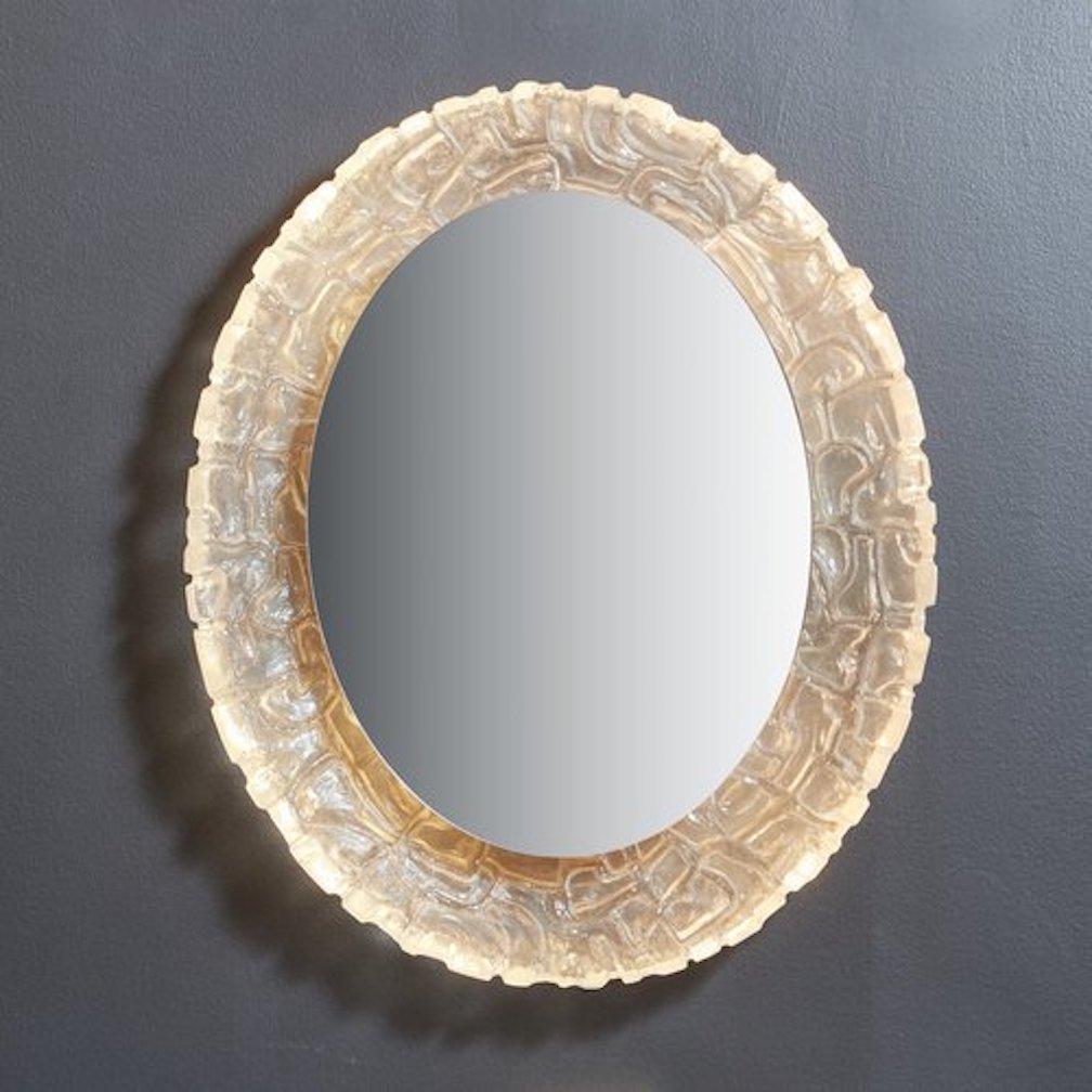 A 1970s German wall mirror attributed to architectural lighting manufacturer Erco. This mirror features a curved molded resin frame with beautiful textural details. It has a backlit oval mirror which appears to float within the frame. When lit, this