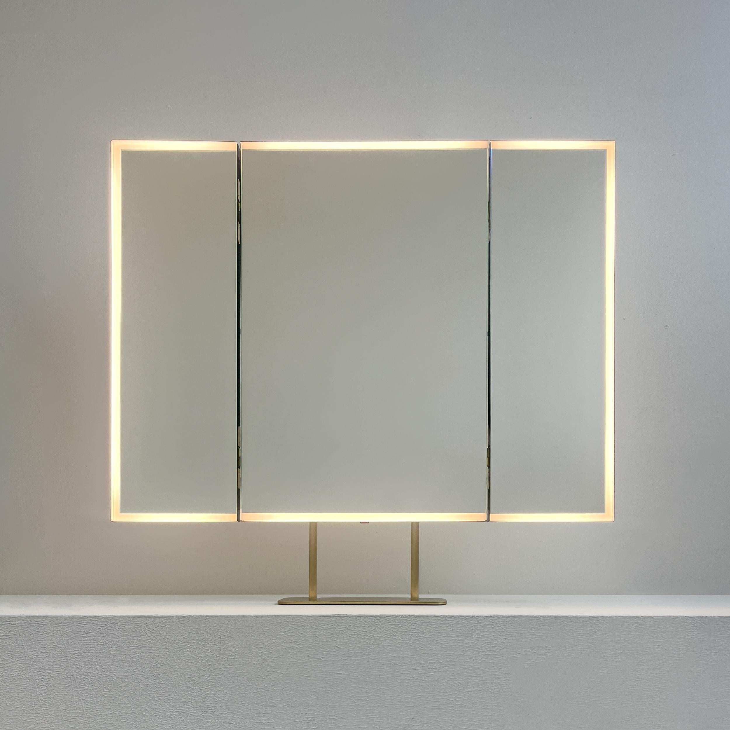 Exquisiter Triptychon-Tischspiegel mit Frontbeleuchtung und minimalistischem, handgebürstetem Messingrahmen und -rückwand. Entworfen und hergestellt in London, UK.

Dieser Triptychon-Spiegel besteht aus drei aufklappbaren rechteckigen Paneelen, von