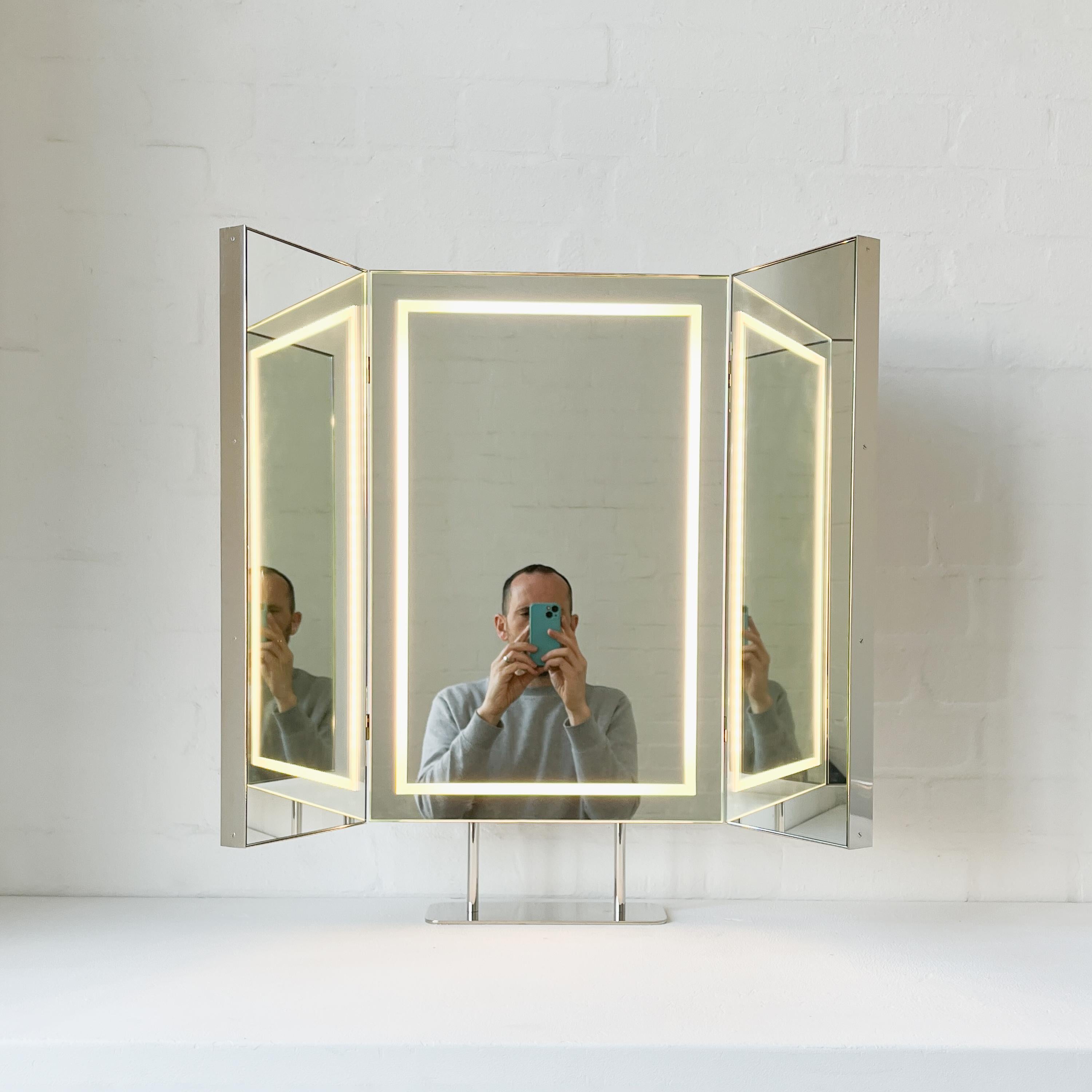 Contemporary triptych countertop rectangular mirror with an elegant nickel plated frame and front illumination integrated in the central panel. Composed of three hinged rectangular panels, the side ones which have 180 degrees of adjustable angle.