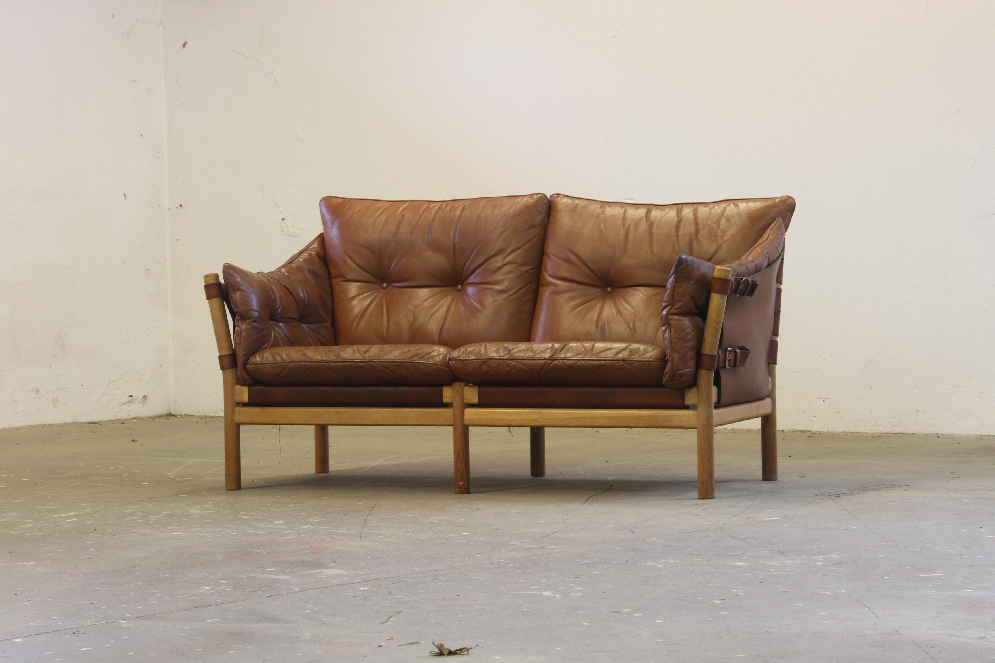 Divano in pelle Maskuline disegnato da Arne Norells negli anni '60, prodotto in Svezia. I cuscini in pelle marrone sono montati su supporti a fascia in pelle con ferramenta in ottone, mentre la robusta struttura in legno di faggio ne esalta la