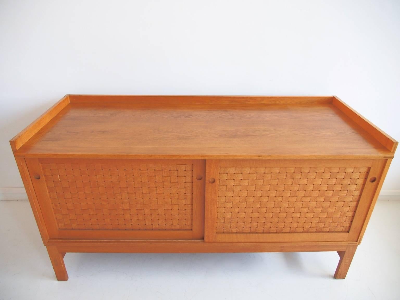Ilse Rix oak sideboard with finger joints and gallery edge. Front with two sliding doors, each with woven wood fronts enclosing solid oak sliding trays, several of which compartmentalized and covered with beige velvet. Produced by Uldum Møbelfabrik