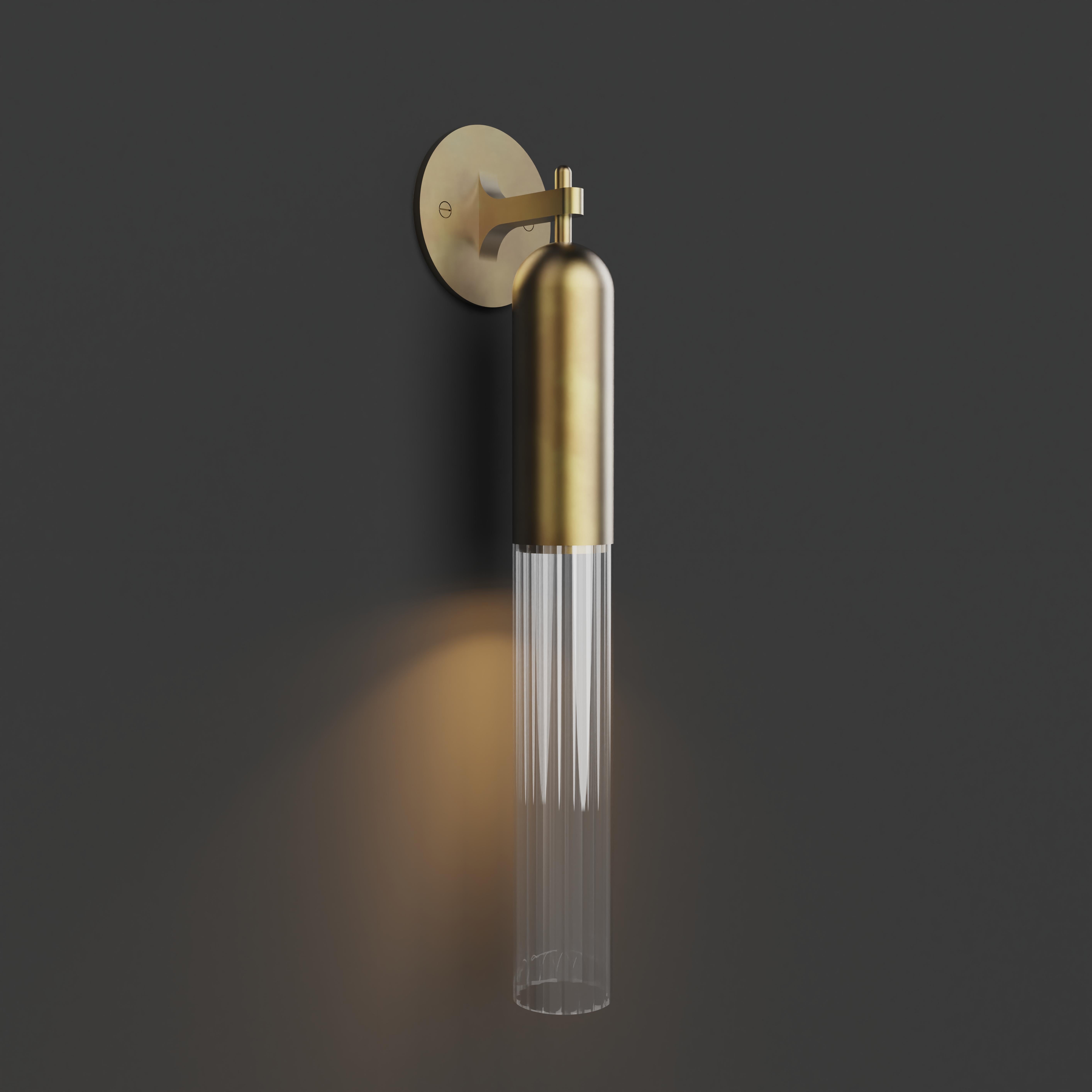 Wall Light in  brushed brass metal finish with fluted glass shade. 

Dimensions:
Overall Height: 450mm 
Glass Dia: 60mm 
Overall projection: 100mm 
Backplate Dia: 110mm
Integrated LED

 Made to order to buyer's specification. Variations to