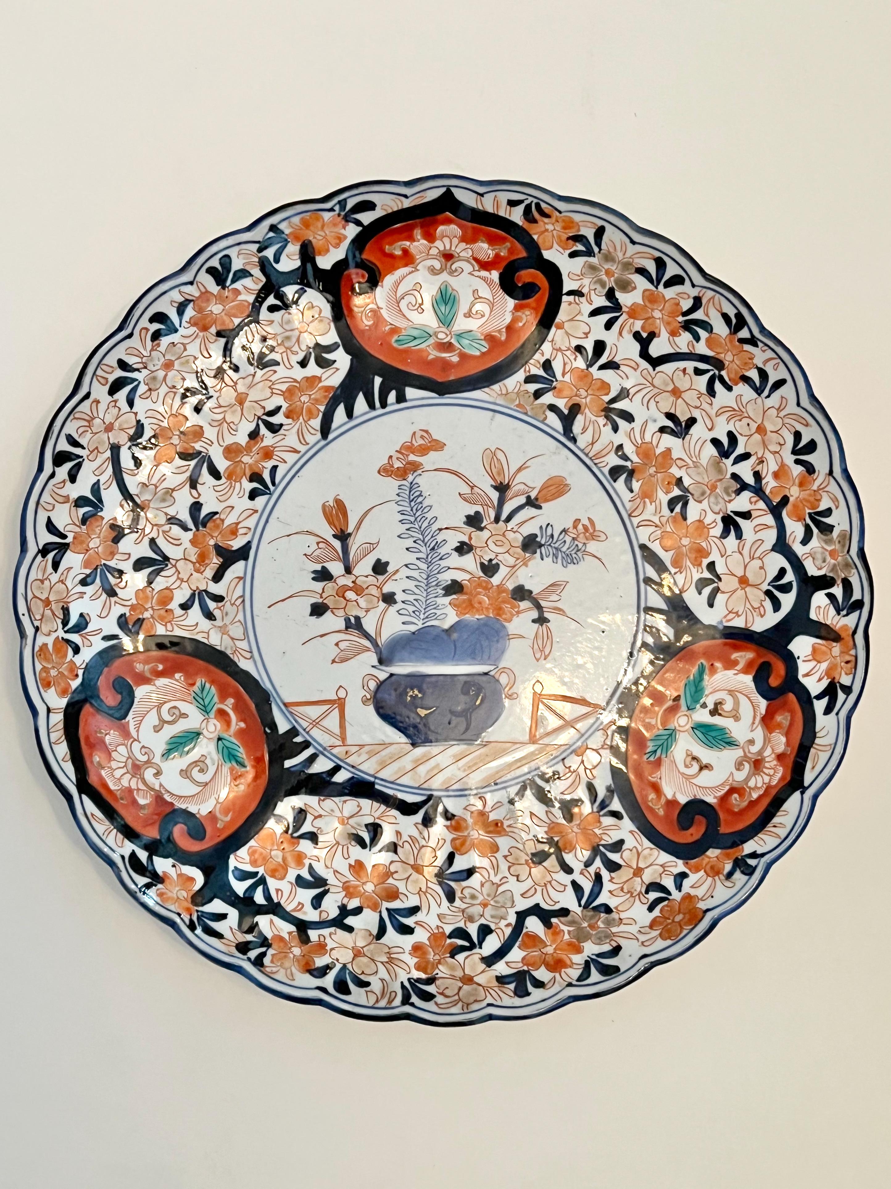 This is a good example of an Imari Charger that features a central basket, small scalloped border with an allover cherry blossom motif with three reserves. The diameter of the charger is 12 inches. The reverse features a scrolling vine design. The