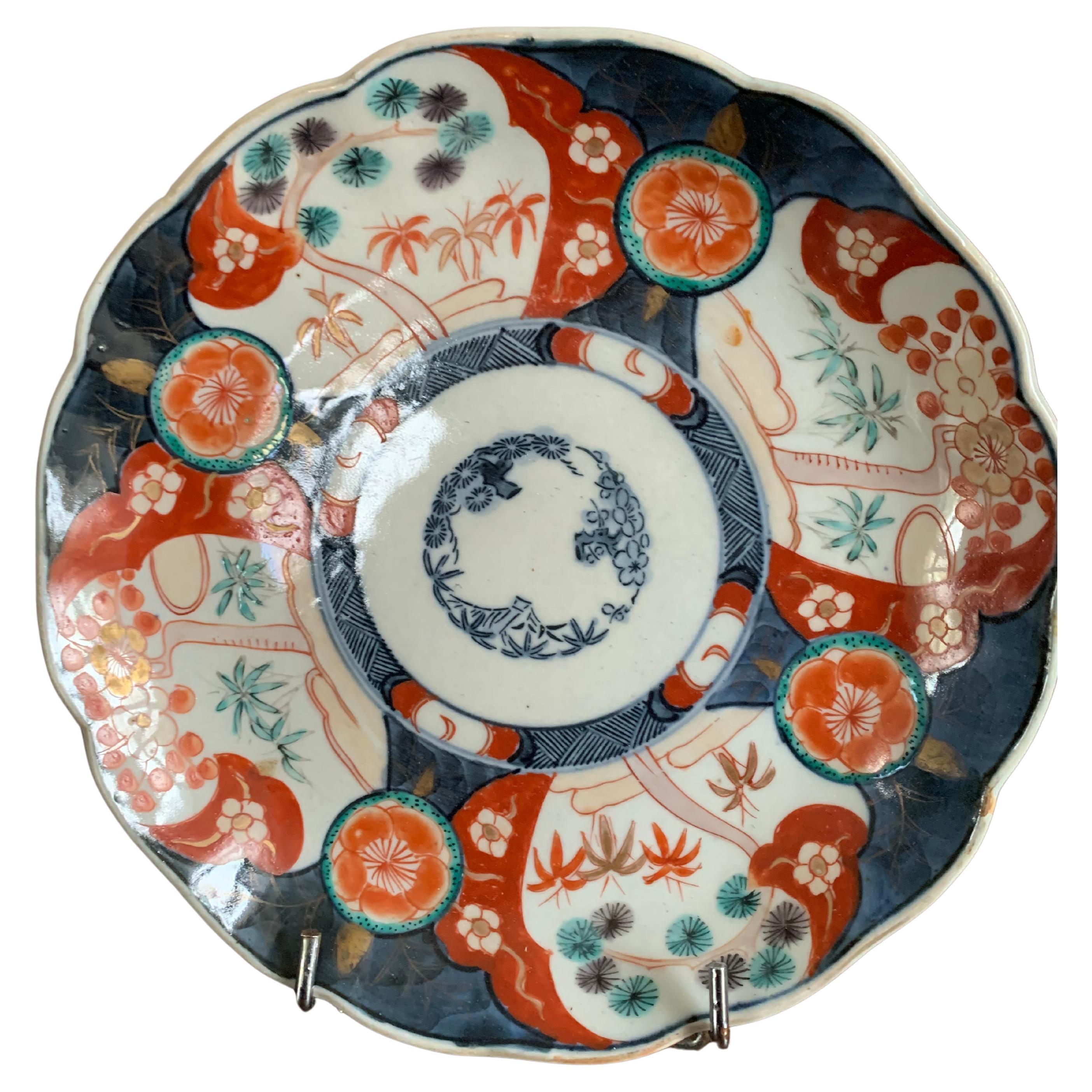 Schöner Porzellanteller mit Imari-Dekor. Auf diesem Teller ist der Hintergrund blau und weiß, mit Reserven, in denen wir rote Blumen und Bambusblätter Muster beobachten können. Imari-Porzellan ist eigentlich eine Produktionsstätte für japanisches
