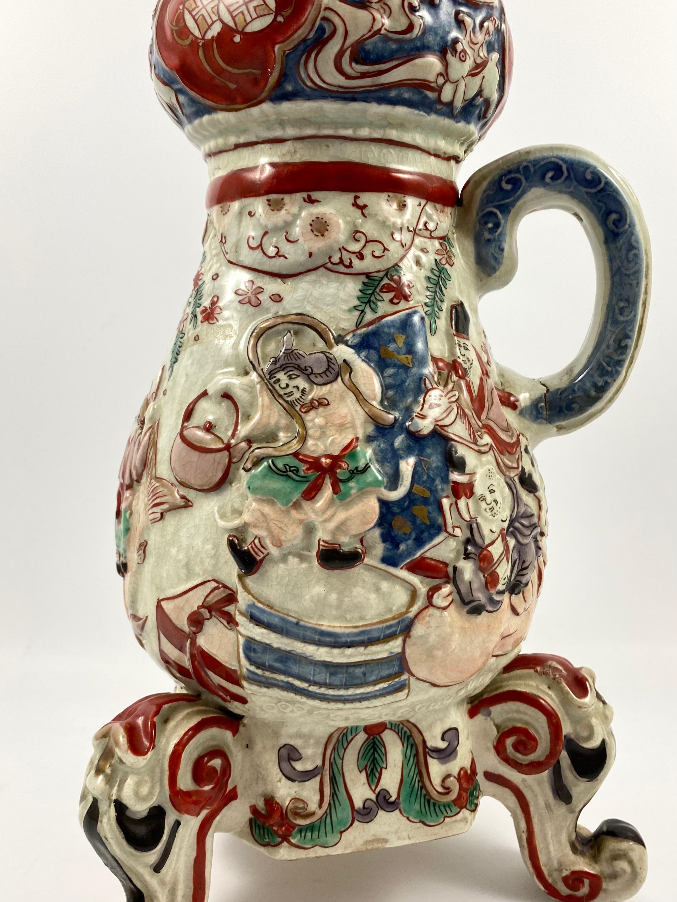 Imari porcelain coffee pot, Arita, Japan, late 17th century, Edo Period. The baluster shaped coffee pot moulded with a continuous scene of Daikoku, Ebisu and Hotei drinking sake, along with various attendants, beneath trees, and a tasselled swag.