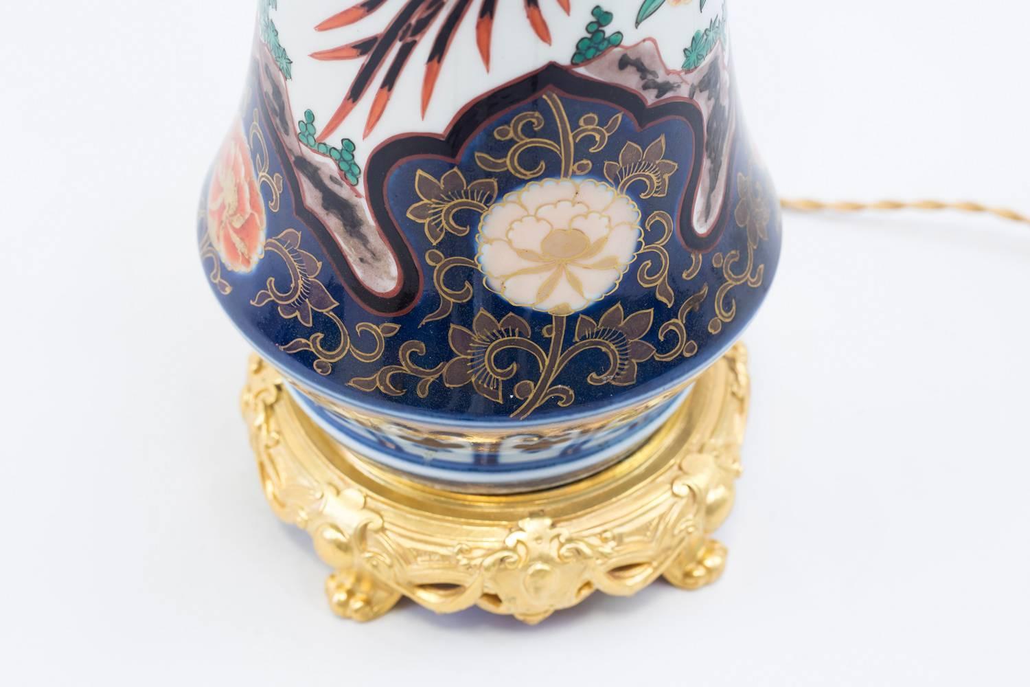 Lamp made from a shortened trumped shaped porcelain vase, an Imari one from the Green family. Vegetal and animal decoration like prunus, phoenixes, an eagle and many flowers like peonies. Truncated dragons are visible on the collar. 
Chiseled and