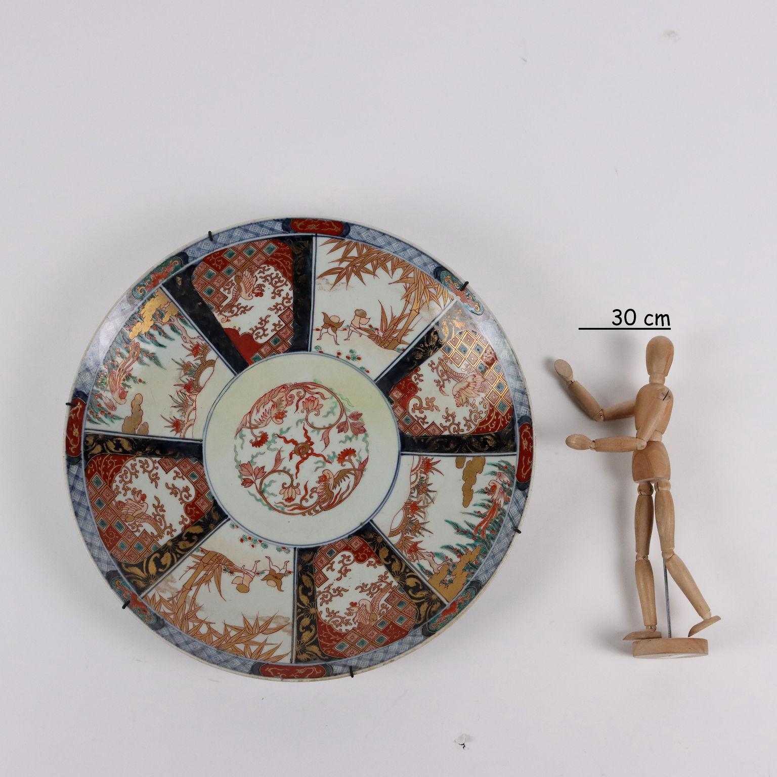 Imari plate in porcelain painted with polychrome enamels, on the bottom in a circle, two opposing phoenixes between plant racemes and a flaming pearl in the center. From a frame to it in a radial scheme within cartouches, various naturalistic