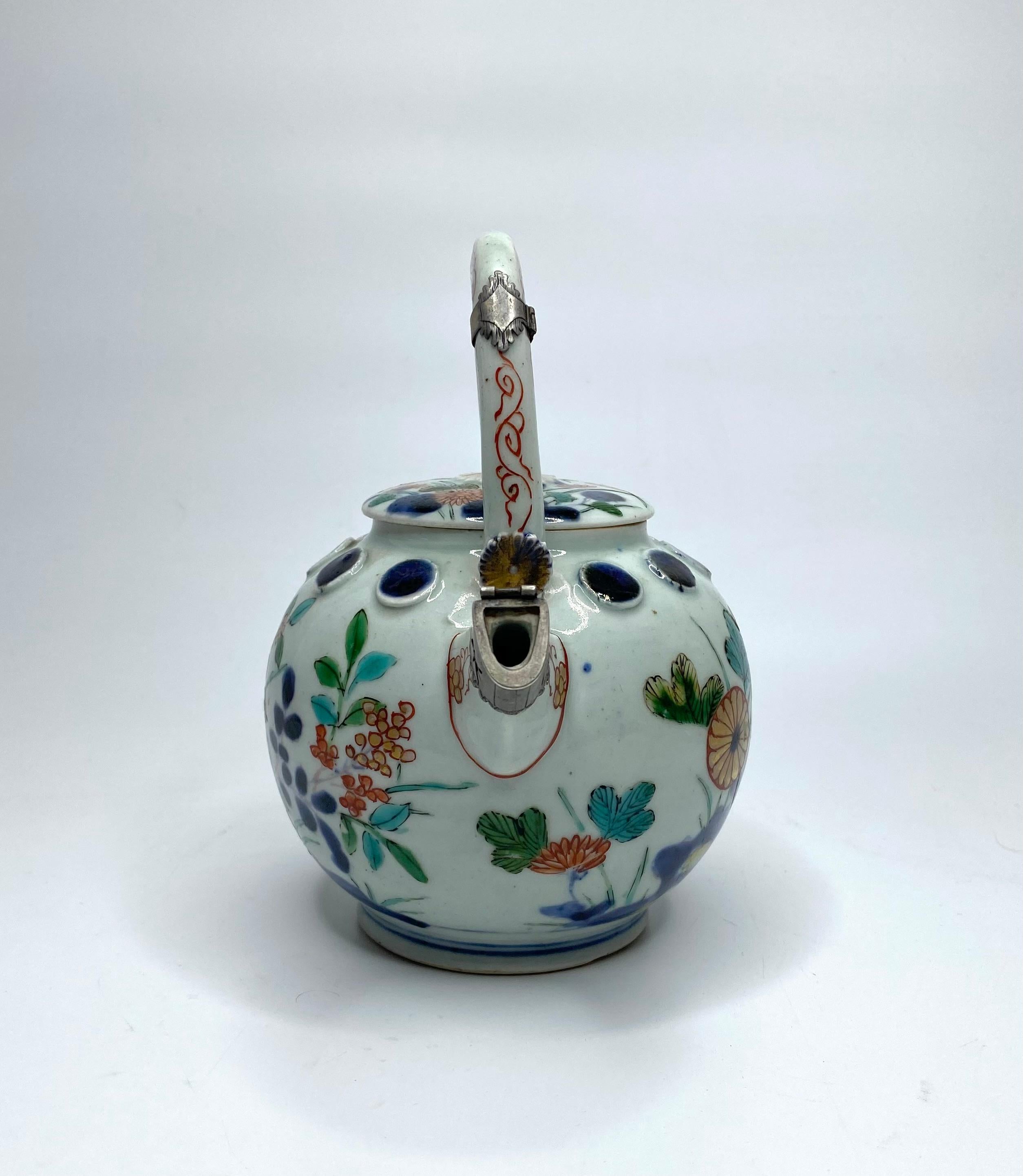 Imari sake ewer and cover, Arita, Japan, c. 1700, Edo Period. The globular ewer, with an unusual continuous band of circular moulded bosses, and vibrantly painted with flowering plants growing around rocks, in typical Imari style, with the addition