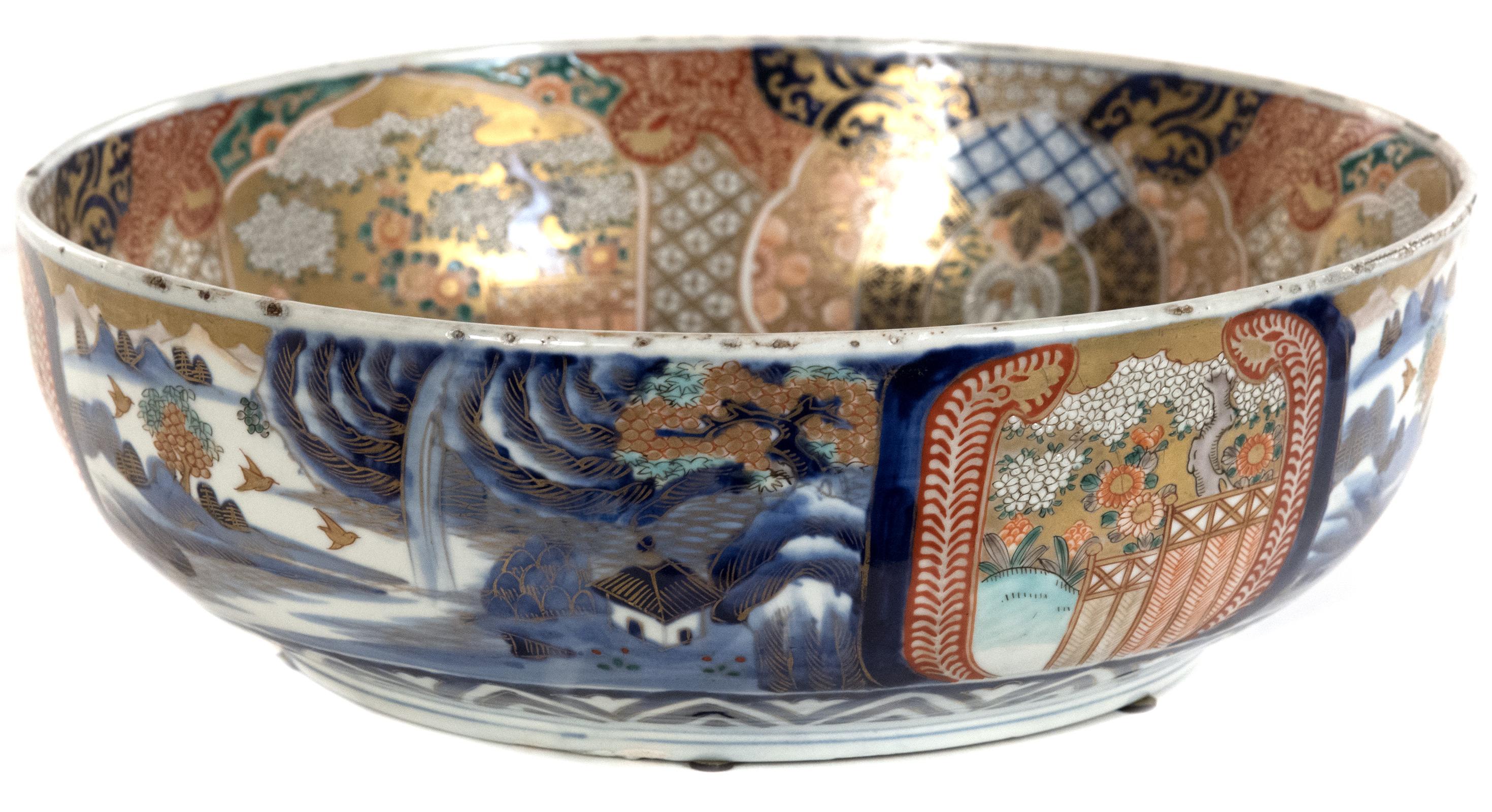 An elaborately decorated Japanese bowl decorated all over in the Imari style that is enhanced with hand-painted gold detailing. The exterior of the bowl is painted with landscapes, with a banded view of a screen and blooming tree, which is copied to