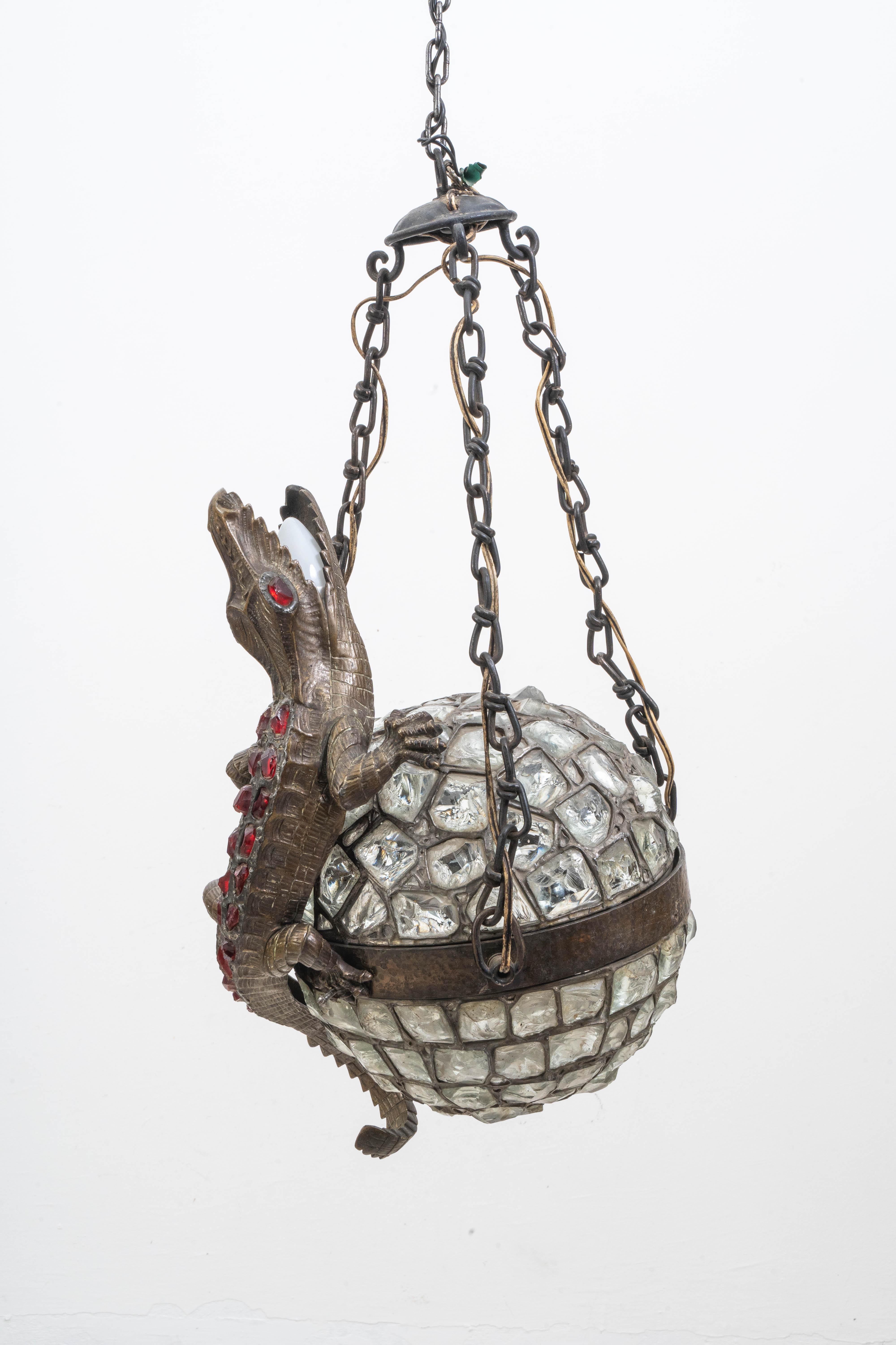 An exceptional and rare hanging lamp featuring a finely detailed crocodile wrapped around a mosaic glass sphere, crafted using the Tiffany technique. The crocodile is rendered with remarkable realism, its body decorated with red glass cabochons that