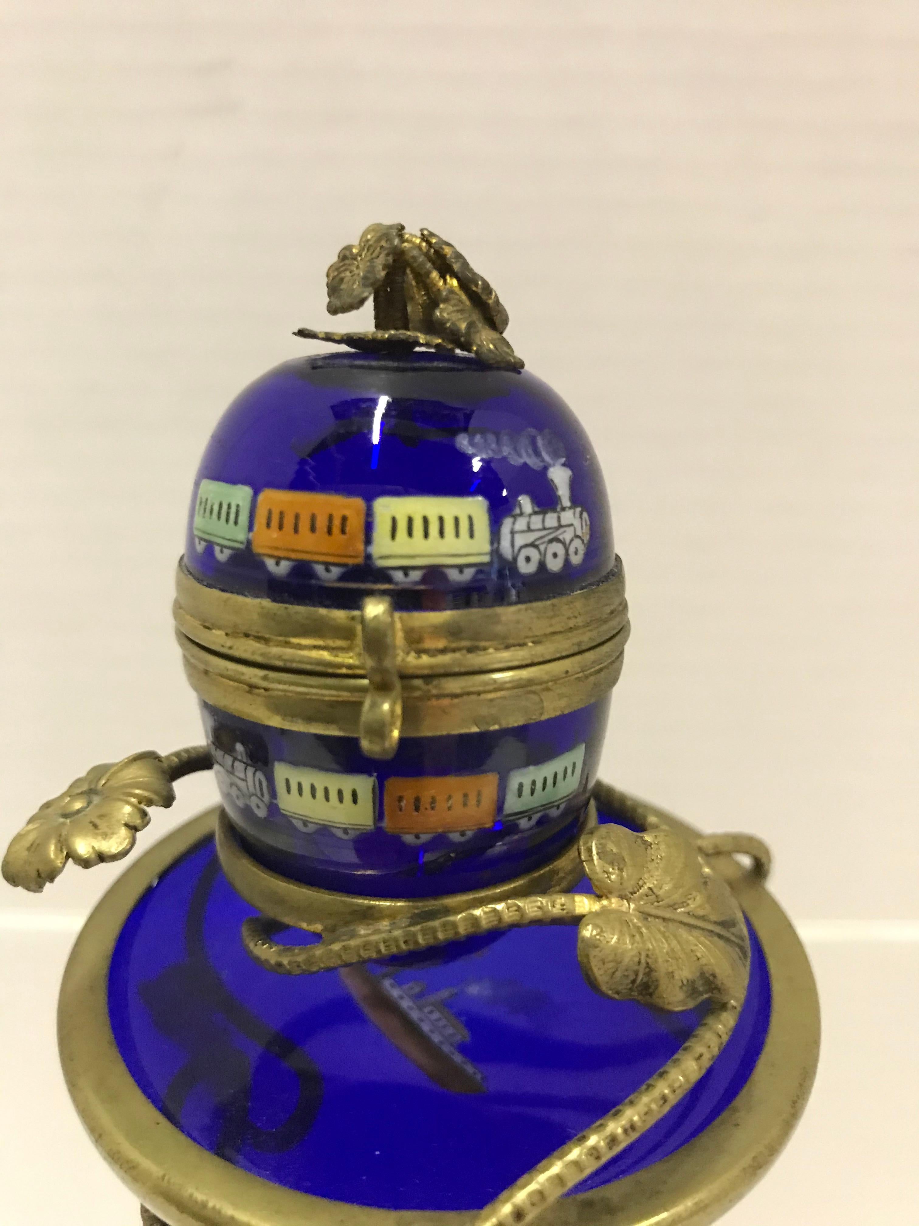 Attributed to the Imperial Glassworks of Saint Petersburg, Russia, an early 1900 cobalt blue glass Egg with gilt stand. Enameled paint decoration with turn of the century trains and steam ship. All this accented with a brass d'ore stand and mounts