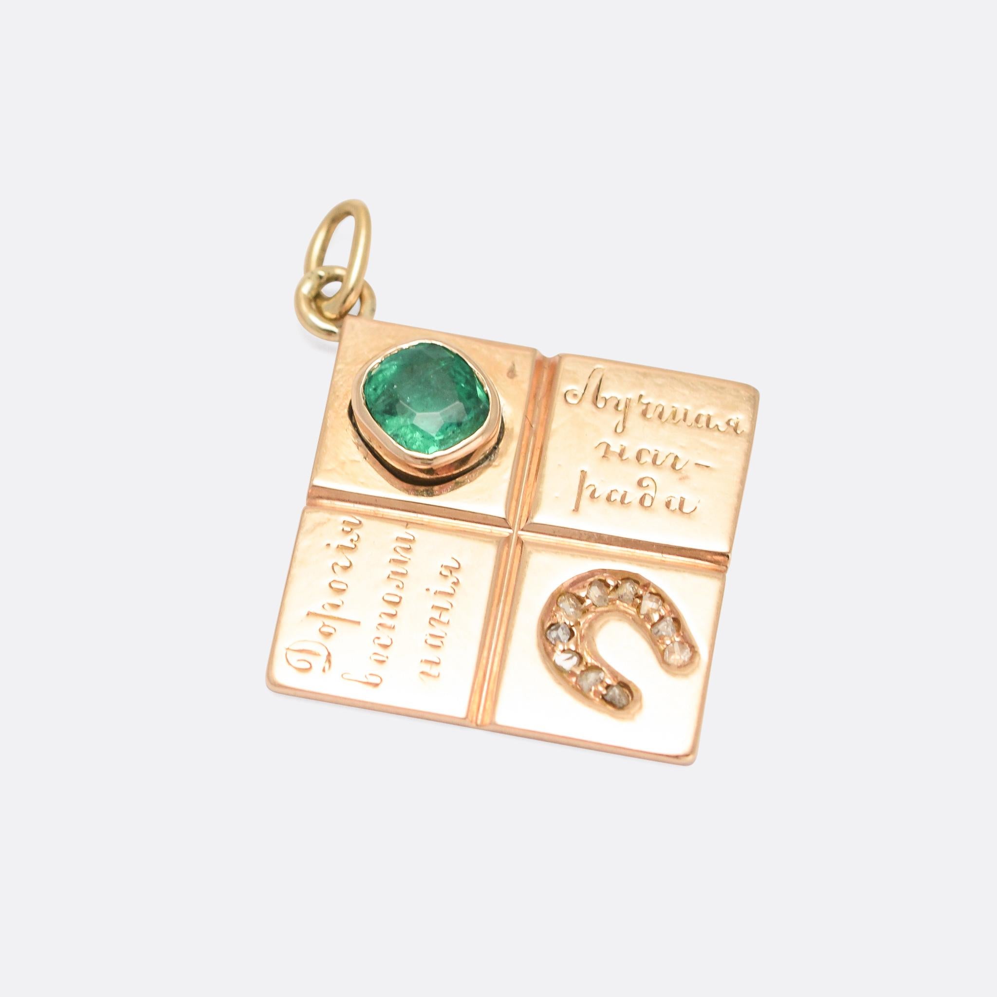 A cool antique Russian lucky charm with four offset square panels: a diamond horseshoe, a vibrant green emerald, and two with Russian text. It's crafted in 14 karat yellow gold, with pre-revolution St Petersburg assay marks. The script is an old