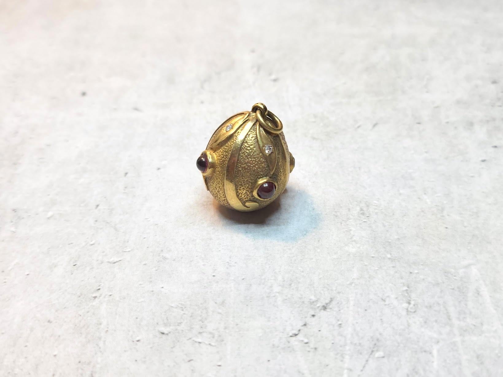 Presenting a rich and finely egg pendant adorned with foliage ornamentation encrusted with four garnets and four diamonds. The body of the egg features hand-engraved yellow polished and brushed gold that creates a fantastic contrast. It is truly an
