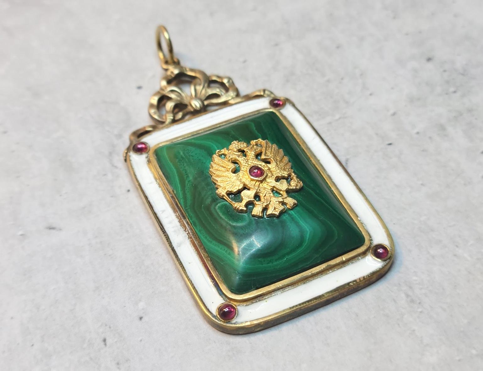 Imperial silver gilded pendant of Russian origin, with malachite inlay and decorated with a double-headed eagle—the Coat Of Arms of the Russian Empire. It is bordered by white enamel and complemented by five small garnet cabochons. 
On the reverse